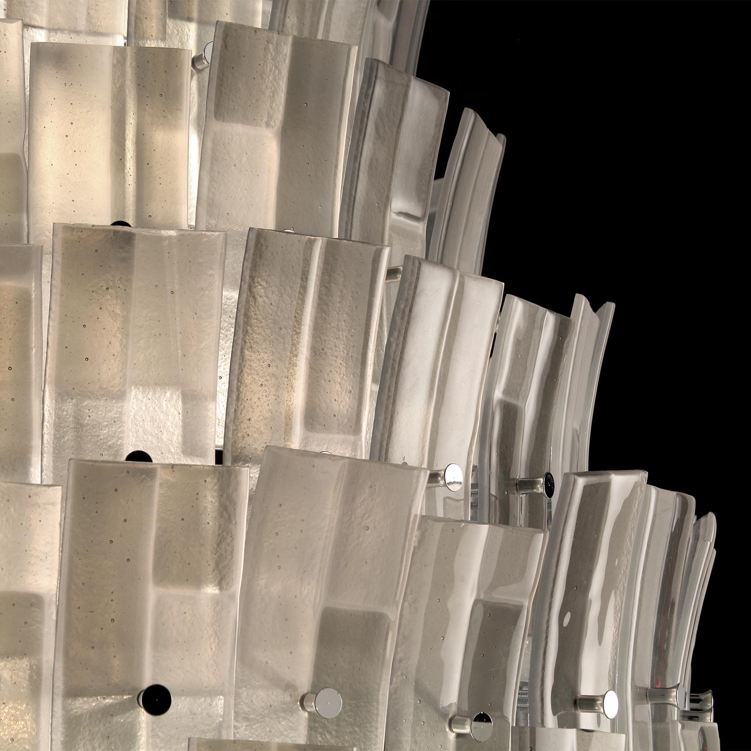 Der moderne Glaslüster Chimera ist unsere Hommage an das Design der 1960er Jahre und seine typischen kreativen Muster. Dieses Beleuchtungsobjekt setzt sich aus modularen Elementen zusammen: Glasleisten in Grautönen, die in einer Kombination