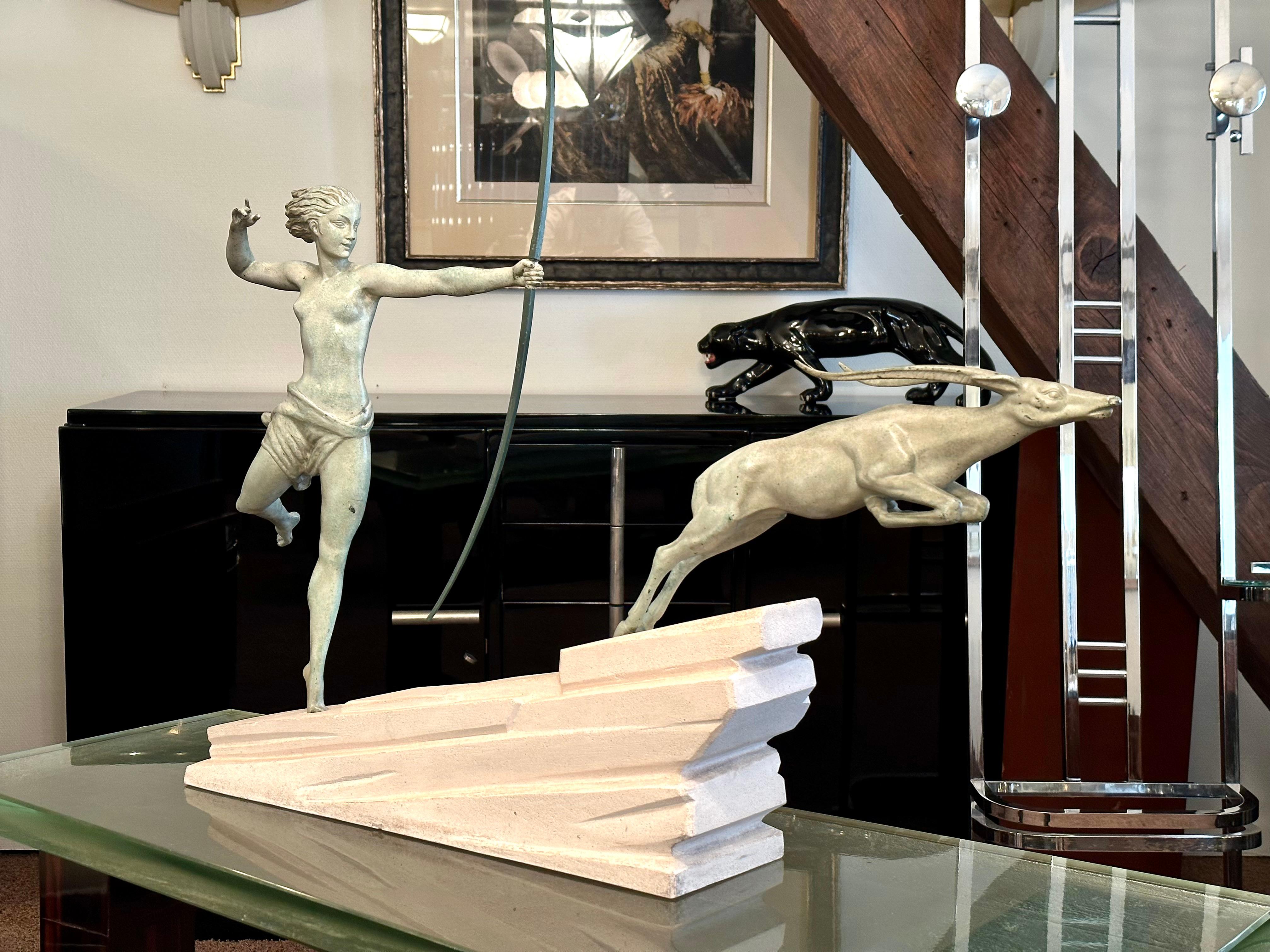 ATALANTE 
Big, dynamic sculpure of a female archer and an antelope.
Colored patinated white bronze. 
Sloping stone base with signature. 

Original work of Jean de Marco for the Max Le Verrier Foundry, early work.
Original Art Deco, France 1930s.