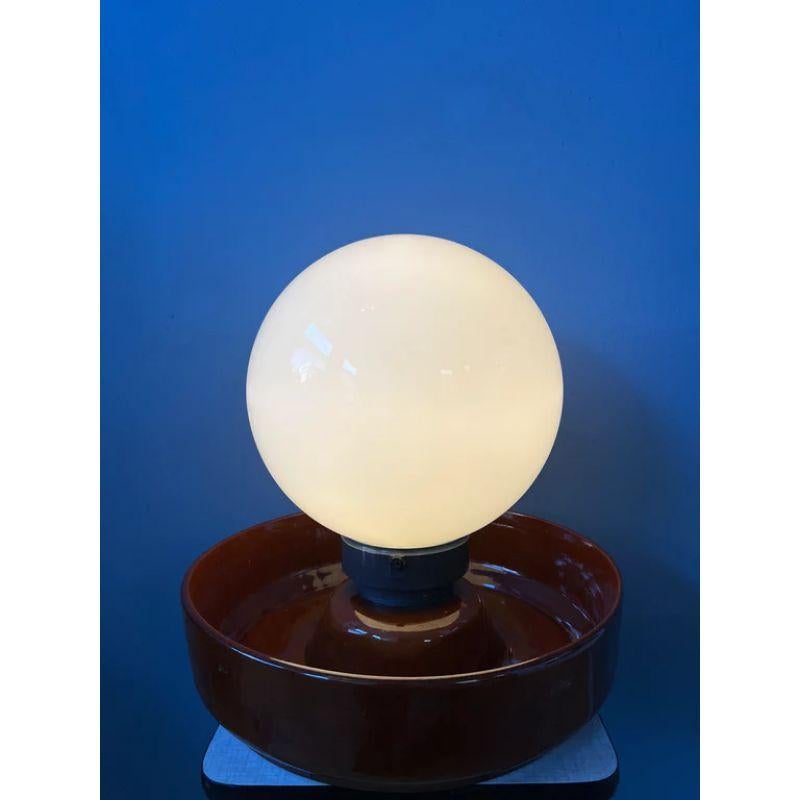 A very big, brown west germany table lamp (and 'bowl') with a big opaline glass shade. The glass shade connects to the ceramic base with three plastic screws on the side. The lamp requires one E17 lightbulb and currently has an