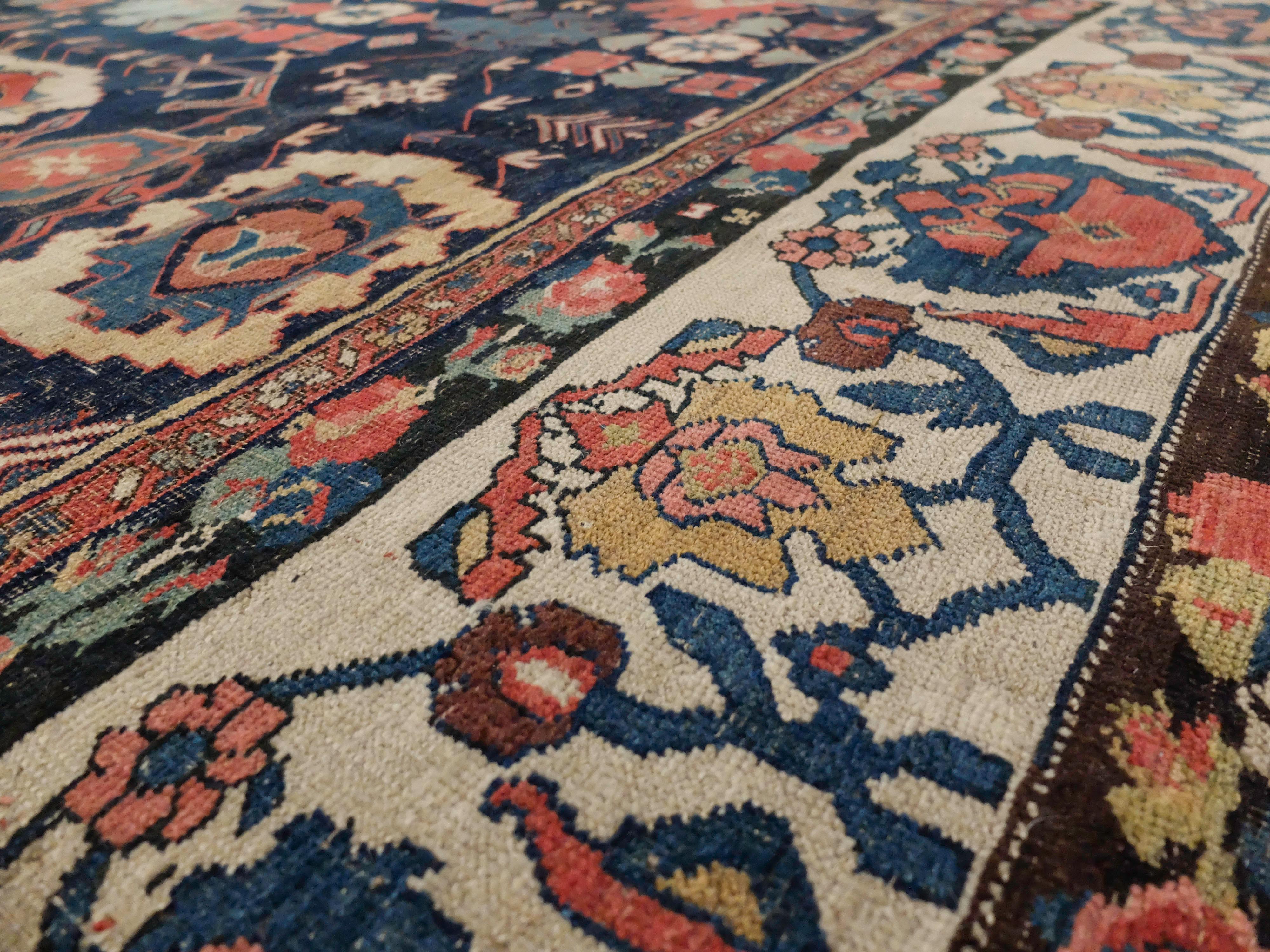 This radiant antique rug has an iconic center medallion surrounded by a sea of intricate symbols and patterns. It has primary colors ranging from indigo, yellow ochre, and Venetian red. A moment of breath is taken in the outer border where it