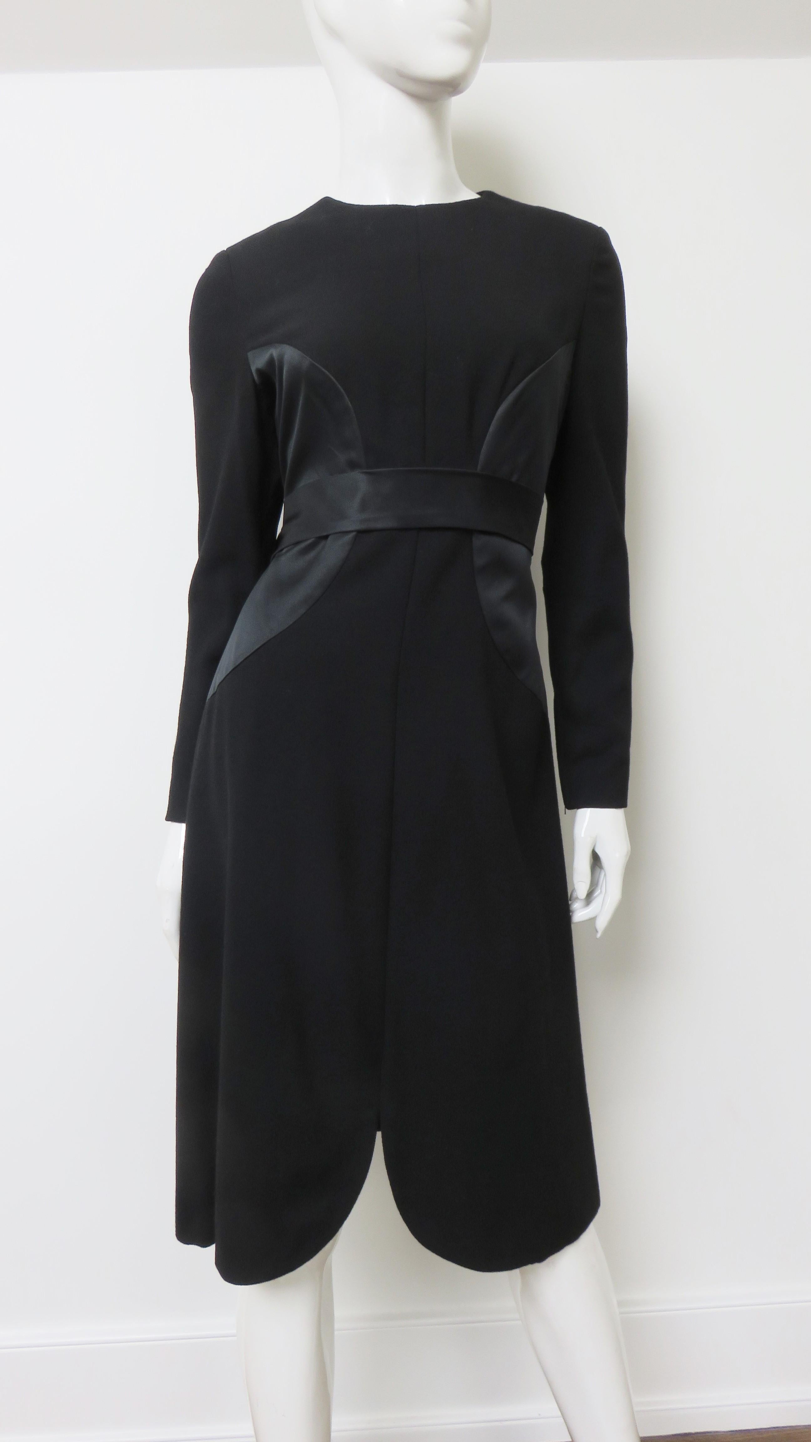 A beautiful black dress from Bill Blass. It has long sleeves with zipper wrists and a subtle A line skirt.  It is semi fitted with large silk circular insets on each side waist matching the silk band around the waist. It is fully lined and has a