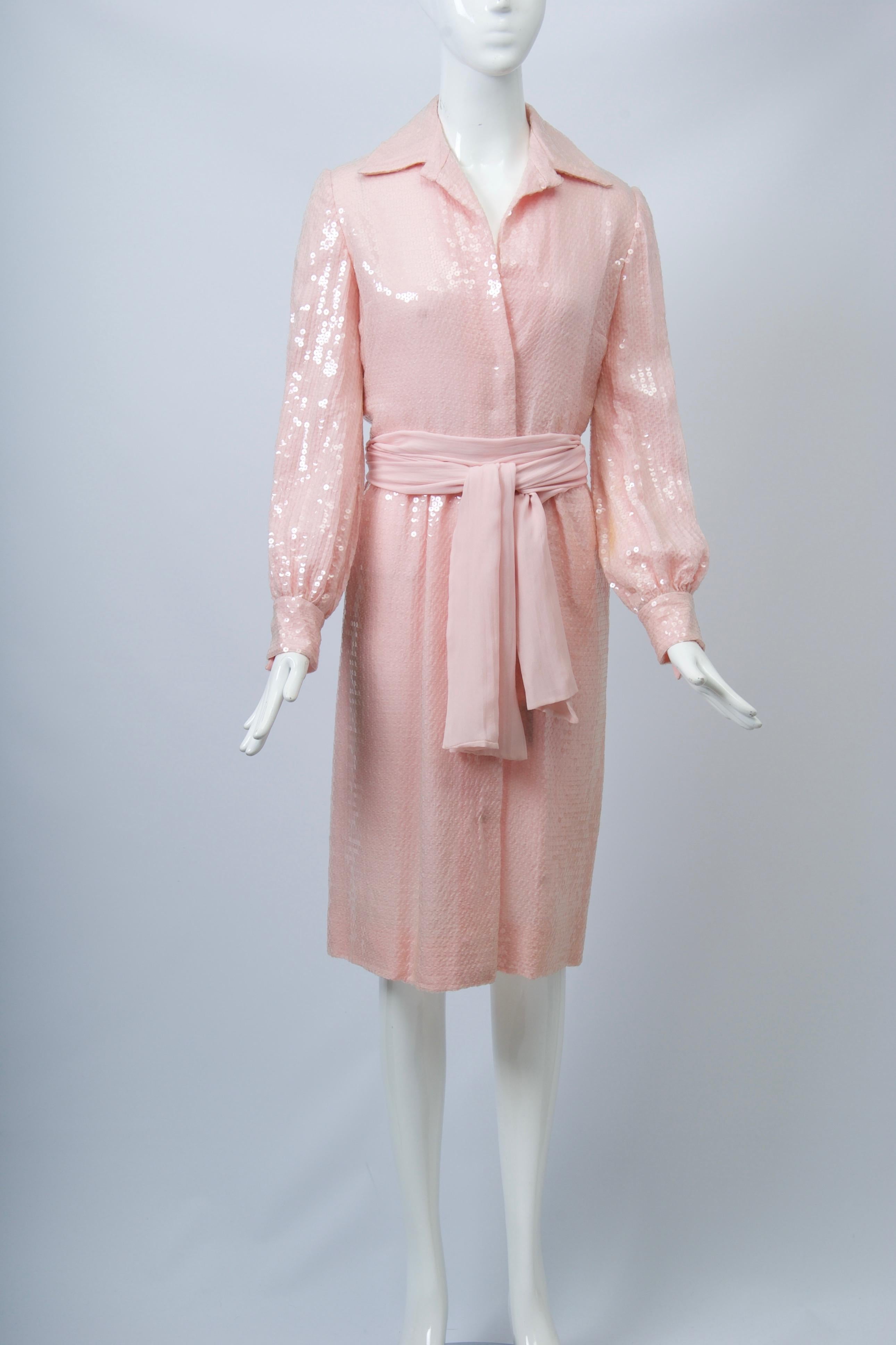 Understated elegance from Bill Blass, this c.1970s evening shirtdress is crafted of  clear sequins on a pink chiffon ground. The dress features a spread collar, long sleeves w/snap cuffs, and a seamed waist finished with a matching chiffon wrap.