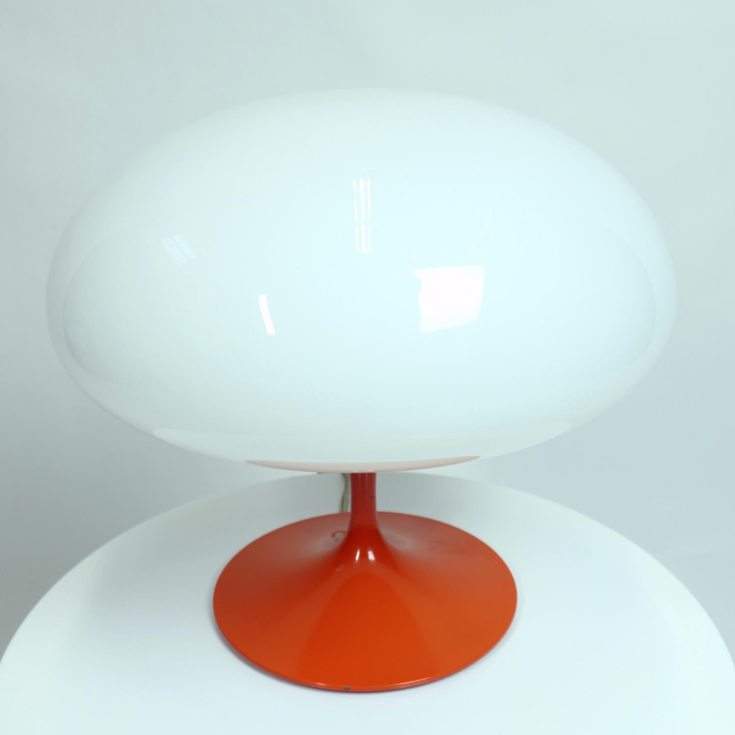 Elevated design is the hallmark of this A-3 Stemlite mushroom lamp by Bill Curry. The table lamp features it’s original deep orange enamel paint. The bulb is shielded by the original, elegant, white glass mushroom dome. The dome rests upon the tulip