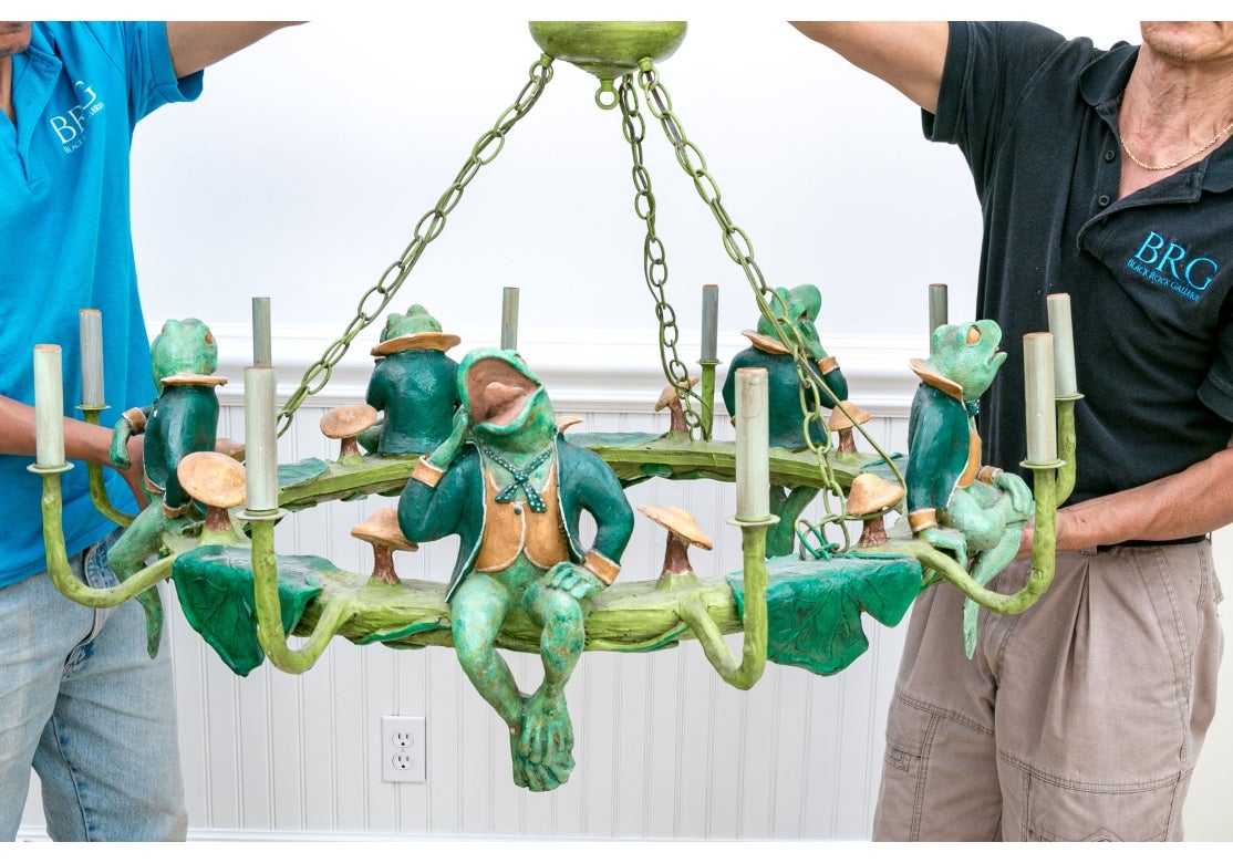 Colorful and very decorative Frog Chandelier by bill Huebbe. The piece is polychrome-painted and showcases five frogs donning vests and coats, perched upon a twig-shaped ring. The chandelier includes ten elegantly upturned faux candle arms, adorned