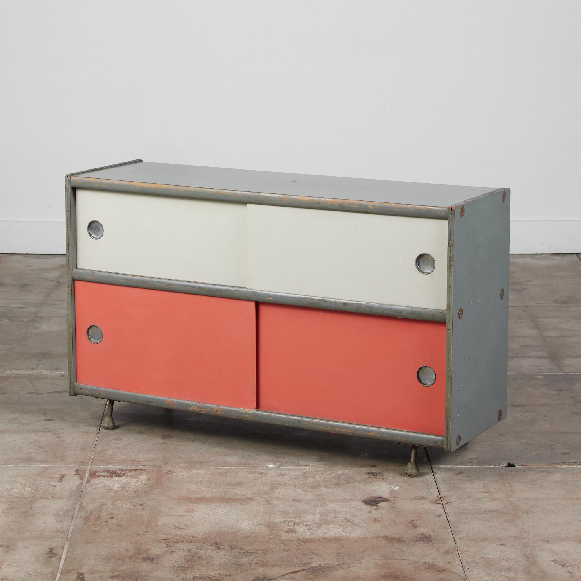 A rare industrial storage cabinet by Bill Renwick for Brunswick, c.1950s, USA. This piece features a gray masonite frame and interior with a laminate top. Both sides of this cabinet have sliding doors in cream and coral which open to reveal shelving