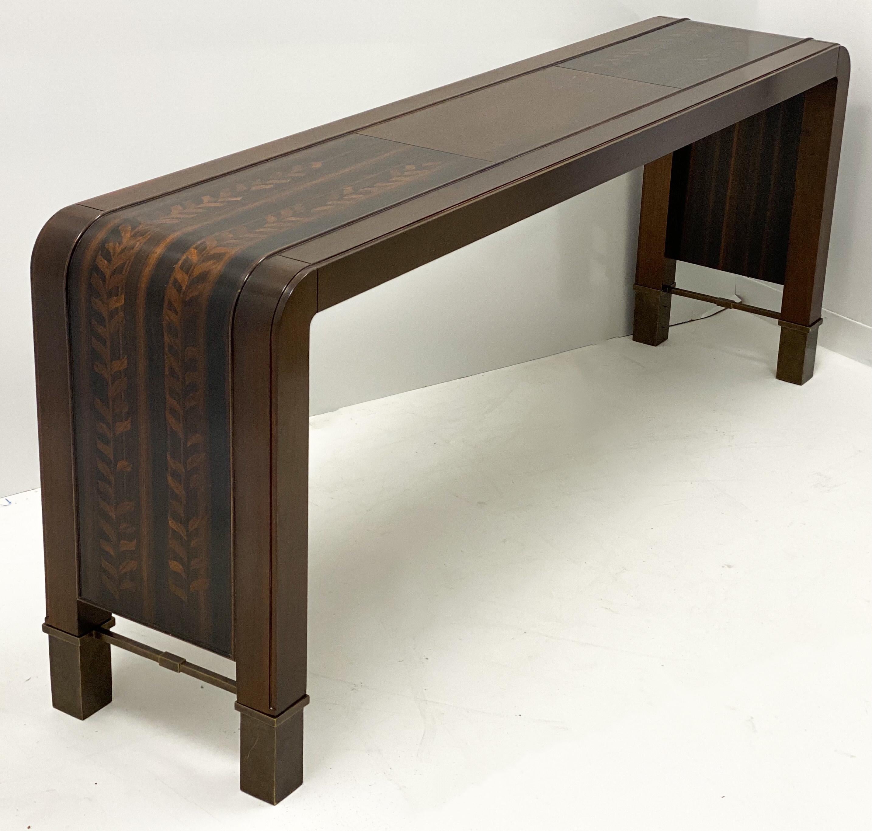 This is a Bill Sofield for Baker Furniture modern waterfall style inlaid console table. It is a blend of mahogany, walnut and satinwood to create almost an aesthetic movement appearance. It has clean lined and bronze cross supports. It is marked and
