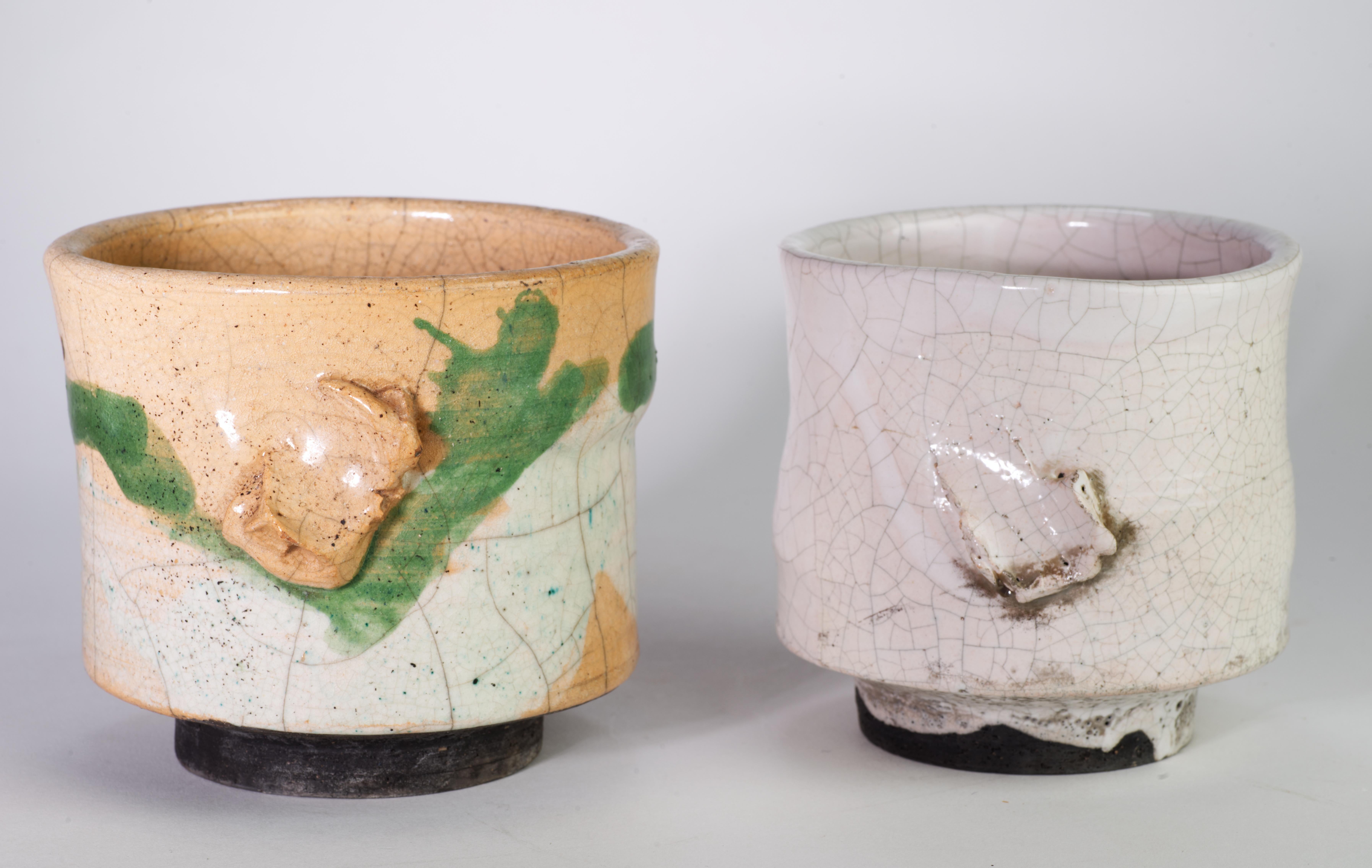  Two sculptural vases or vessels are free-formed by hand and glazed in complex, semi-gloss crackle glaze; matte graphite-colored glaze was used on the bottom parts of the vessels. Both pieces are decorated with abstract relief in front. The smaller