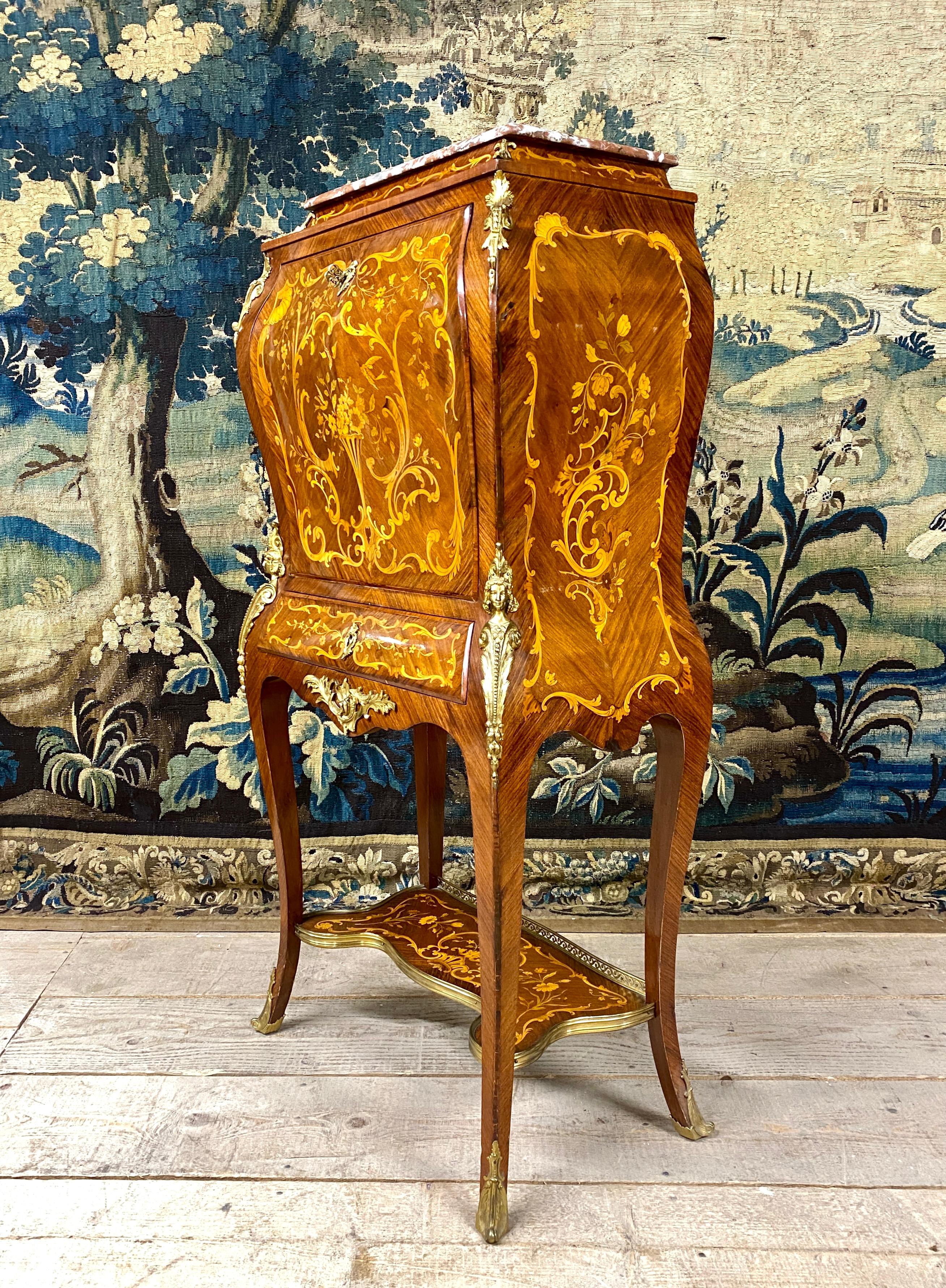 Petit carnet de bonbons en marqueterie et bronzes dorés ouvrant par un abattant, gainé de cuir et ouvrant sur quatre petits tiroirs, ainsi qu'un grand tiroir en façade. Magnifique marqueterie décorée de coquillages, de feuillages, de fleurs et