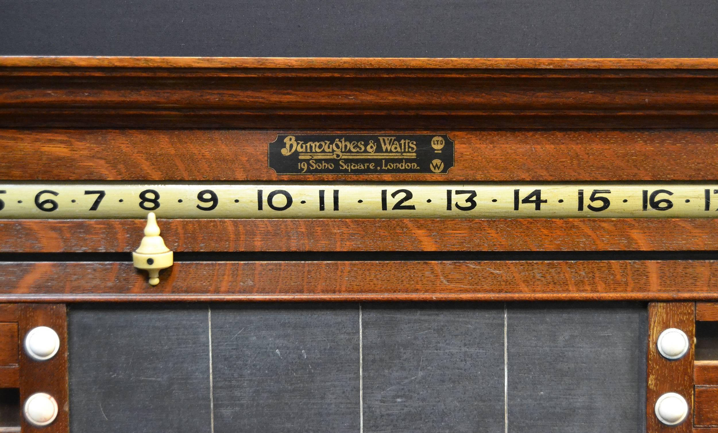 A solid oak combination scoring board by the original Burroughes & Watts Co. of London, circa 1900, central slate panel, flanked by sliding lettered panels for the game of Life pool and revolving number bars allowing each player to score from 1 to