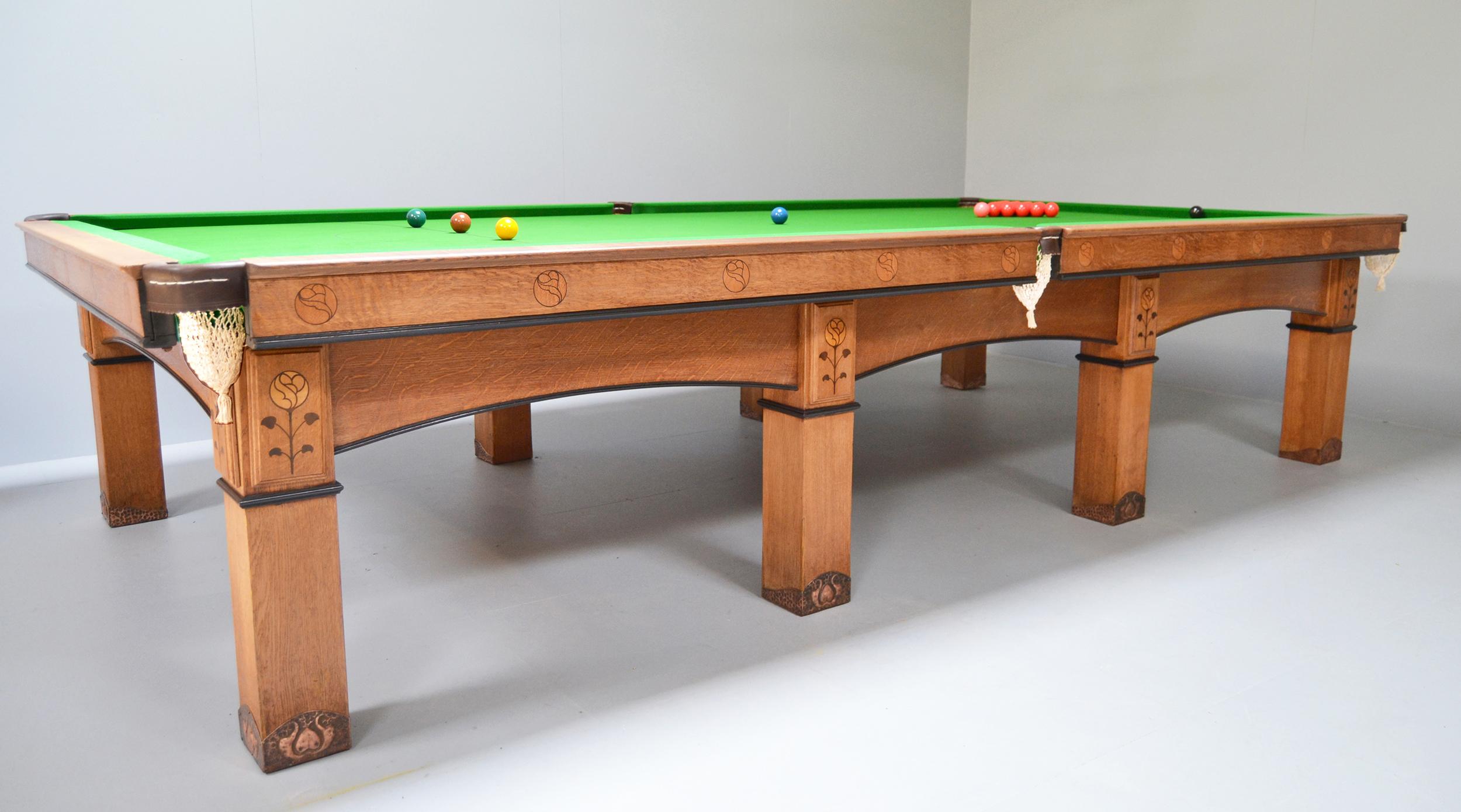 A solid oak full size Arts & Crafts Billiard, Snooker or Pool table, circa 1910 in the style of George Montague Ellwood and manufactured by Burroughes & Watts of London.

Standing on eight substantial oak legs with embellished handmade copper feet