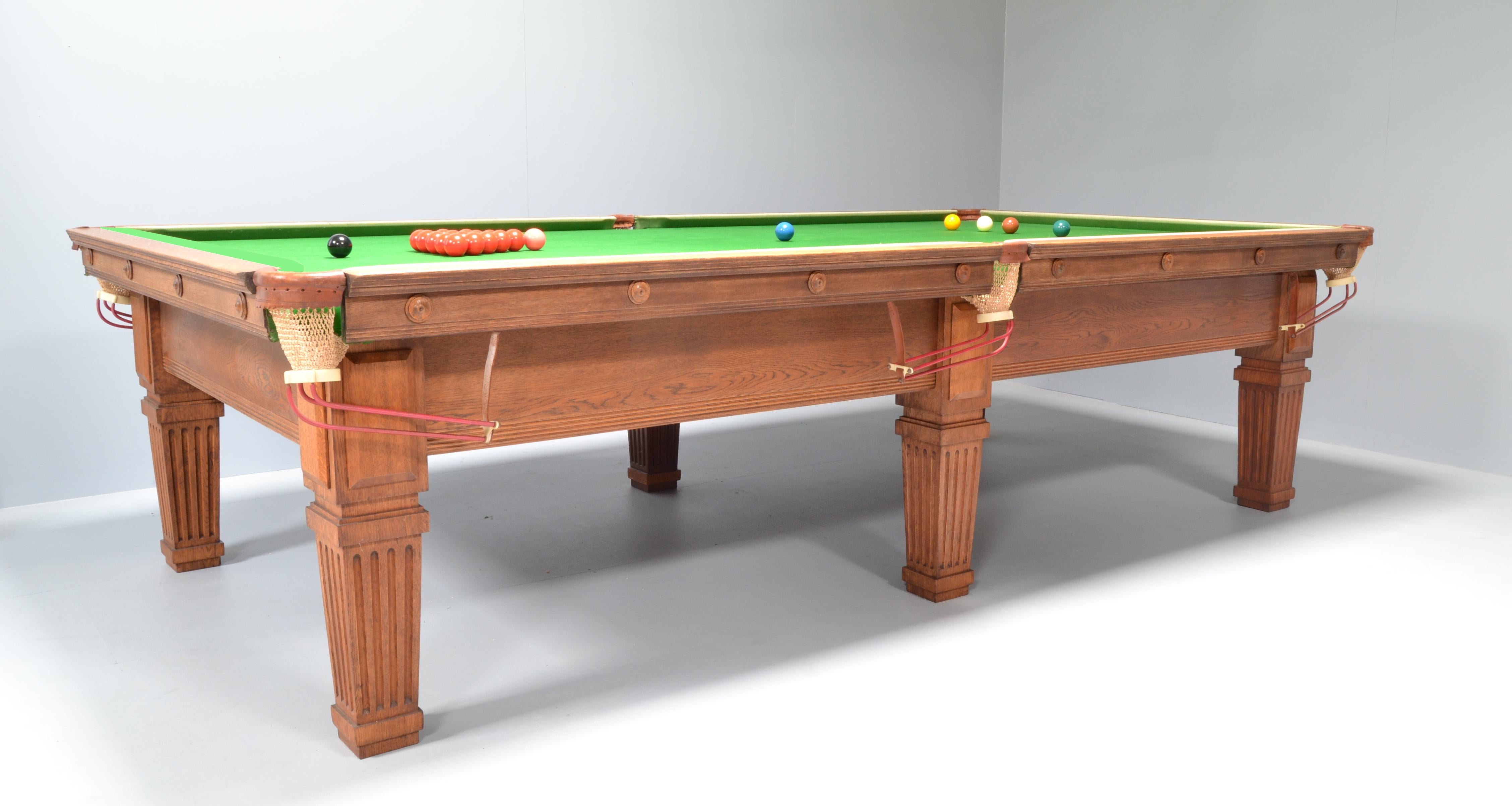 An attractive and very well made solid oak antique billiard or snooker table by Thurston of London circa 1910, standing on six tapering fluted or scalloped legs with applied rectangular cover panels, the cushions with applied decorative roundels.