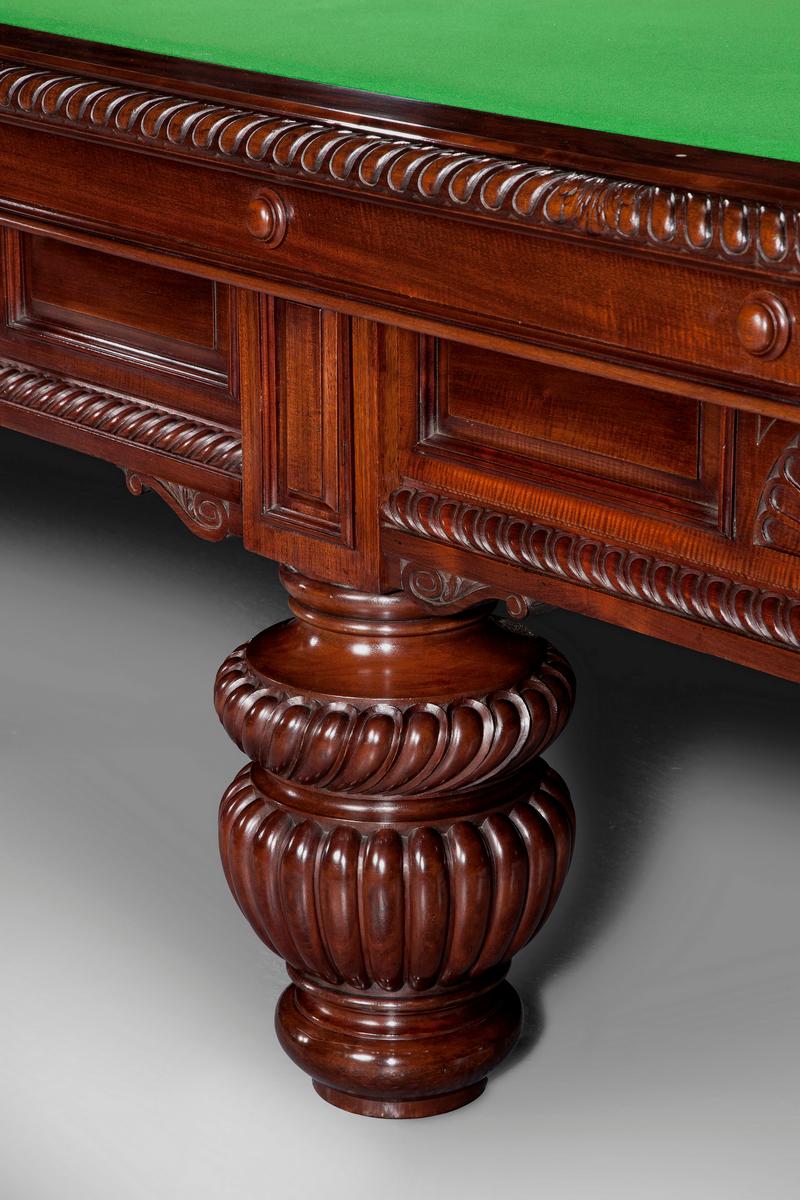 A full size 12ft x 6ft mahogany billiard table standing on eight massive lobed and turned legs, the panelled side frames are embellished with gadrooned mouldings, fan shape carvings and corbel brackets. The intricate cushion friezes compliment the