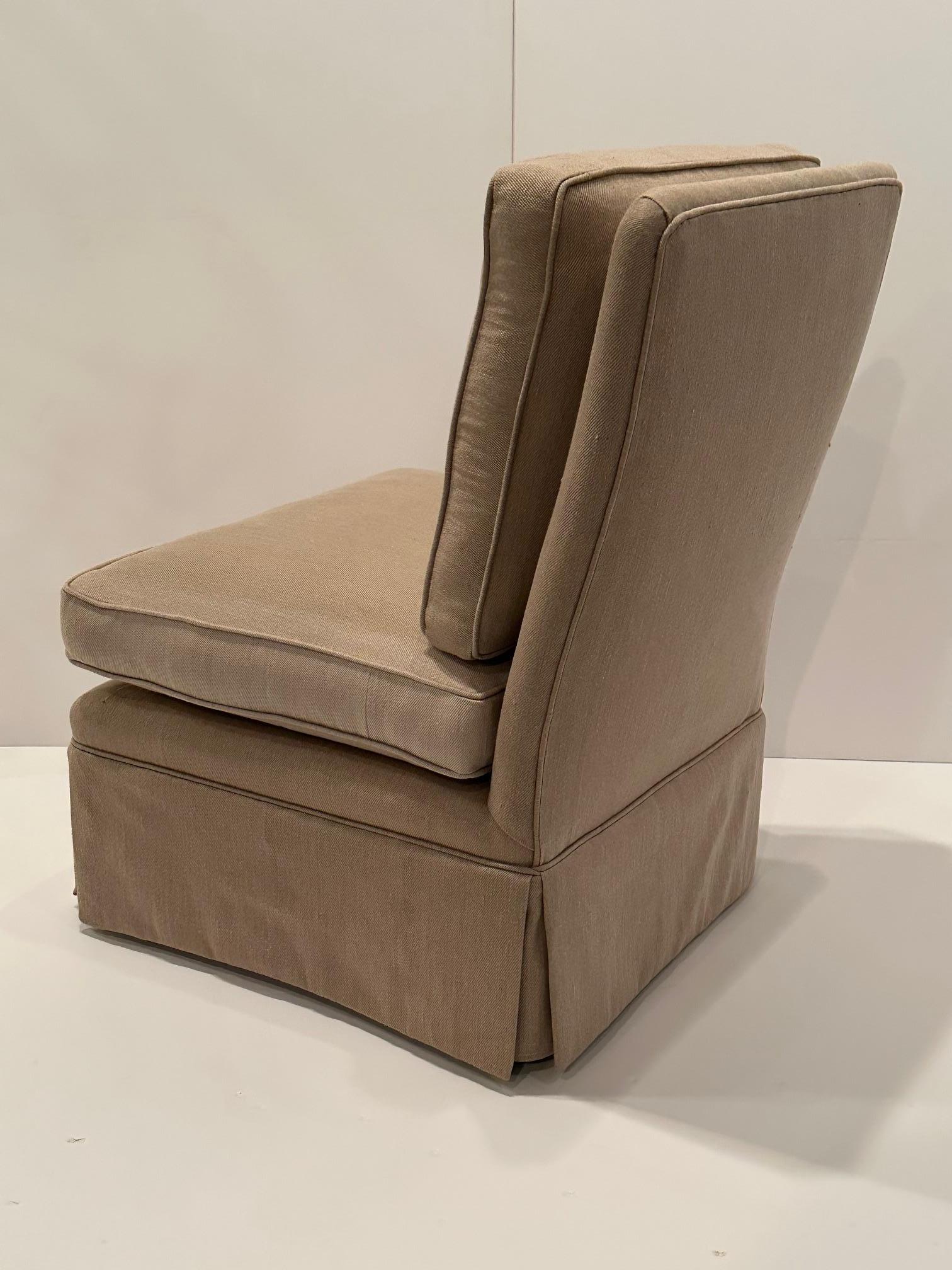 Silla deslizante de estilo Billy Baldwin, clásica y sofisticada, tapizada en tela de lino de color tostado neutro, con pliegues en caja y patas torneadas ocultas de madera oscura.