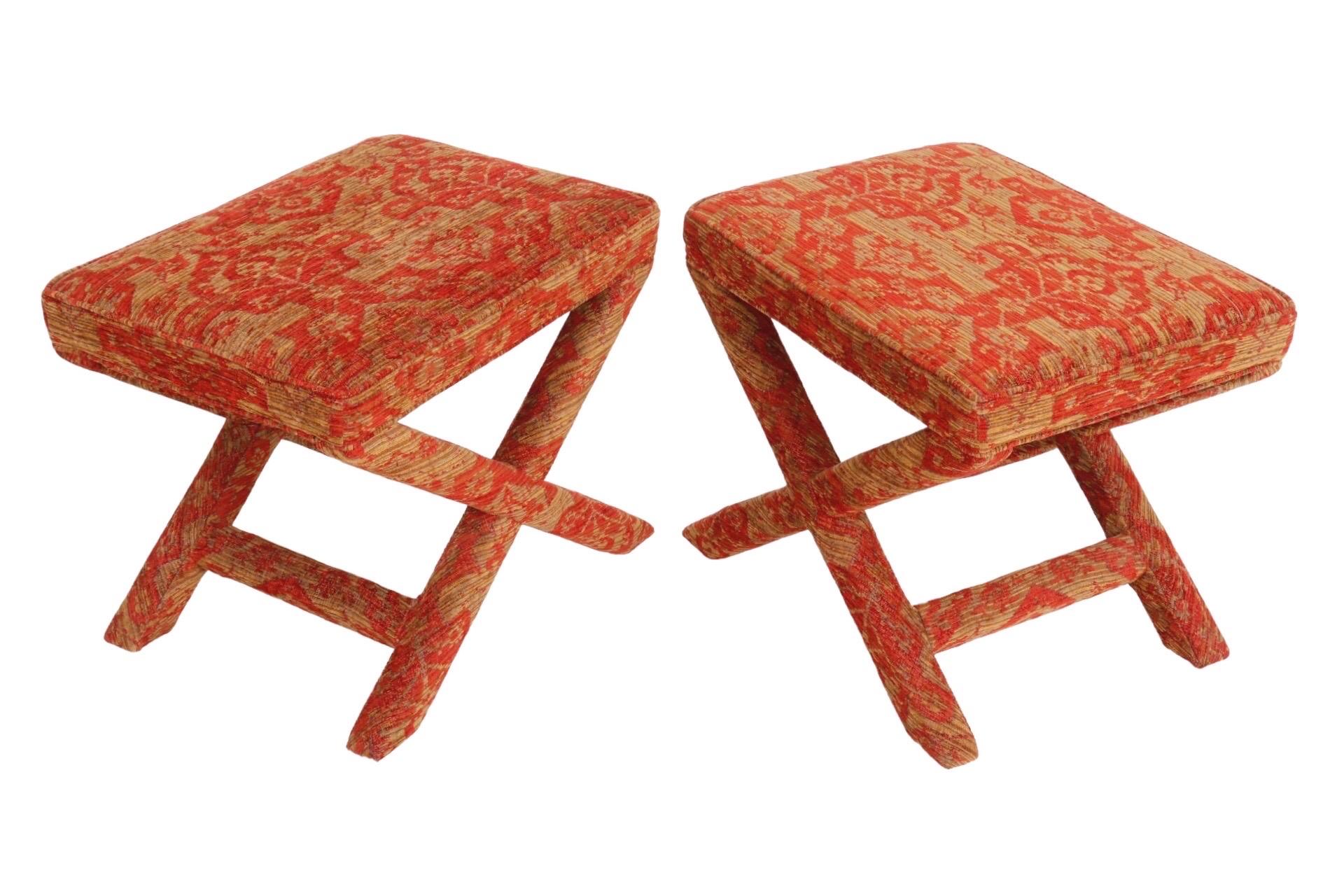 A pair of upholstered ottomans made by Sherrill Furniture, in the style of Billy Baldwin’s iconic X-base ottoman. Rectangular bench ottomans with x shaped legs supported with stretchers are covered throughout in a bold red and gold tapestry jacquard