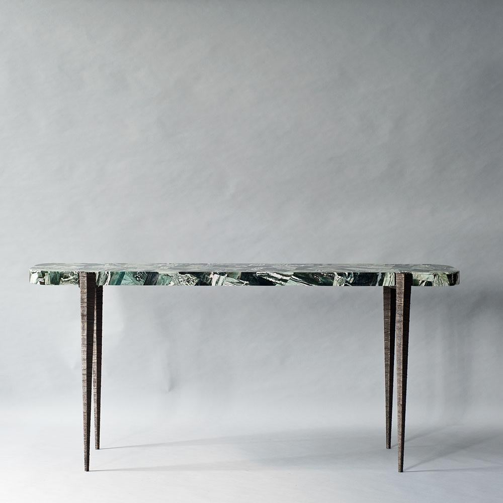 The Bind console by DeMuro Das features a striking stone top in green zebra agate, a lesser-known variety with distinctive green, black, and cream striping. The top is supported by elegantly tapered and textured hand-cast legs in solid antique