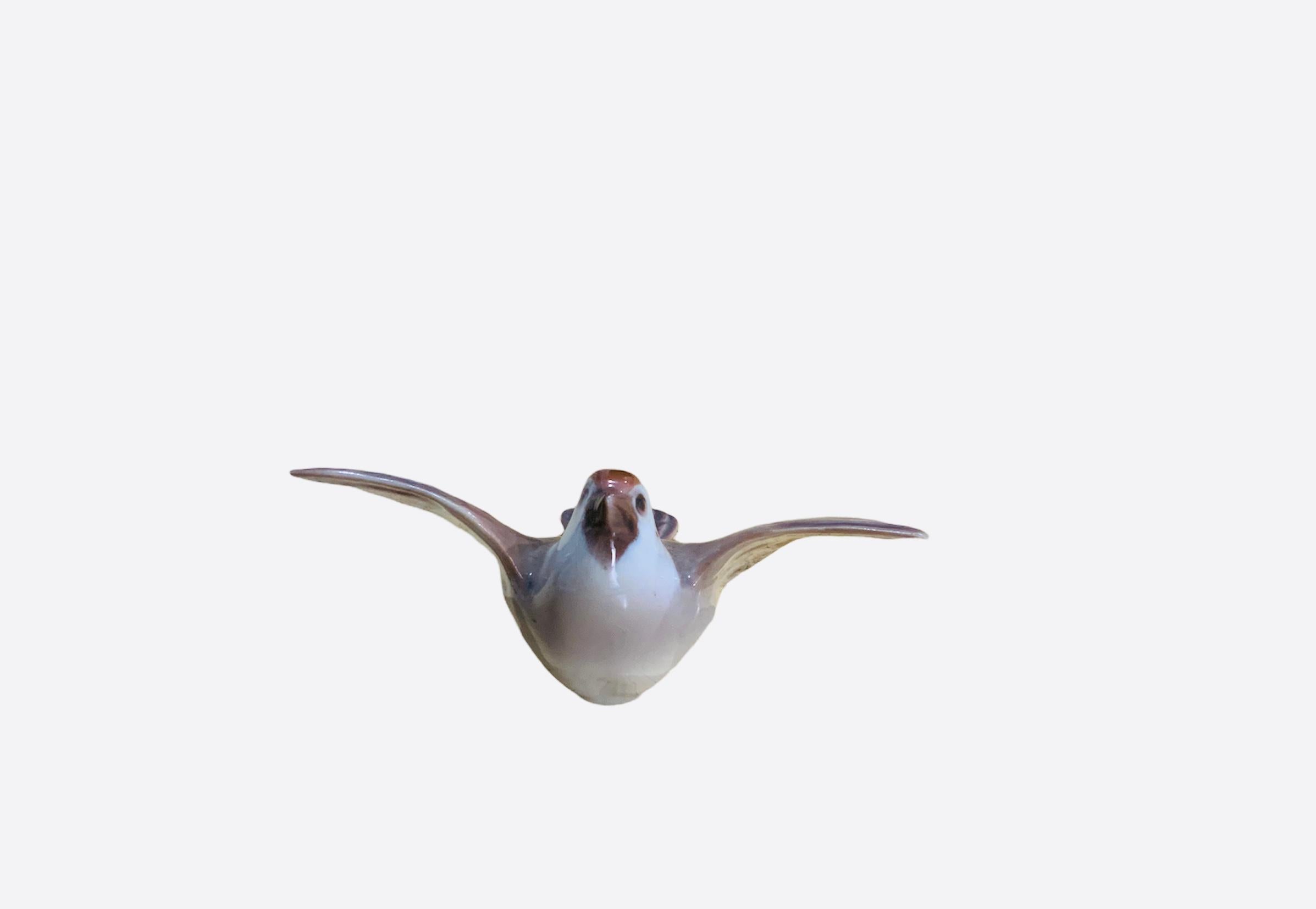 This is a Bing and Grondahl porcelain of small happy bird figurine known as a sparrow. It’s wings are wide open and ready to fly up. At the base is the Bing and Grondahl hallmark with the number-2491 and the letters FO. It is hand painted white and