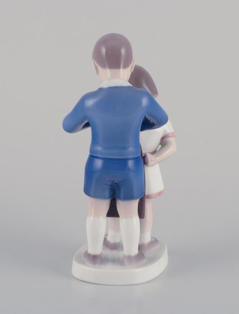 Metà XX secolo Bing e Grondahl, statuetta in porcellana. Ragazzo che aiuta la ragazza con la sua giacca. in vendita