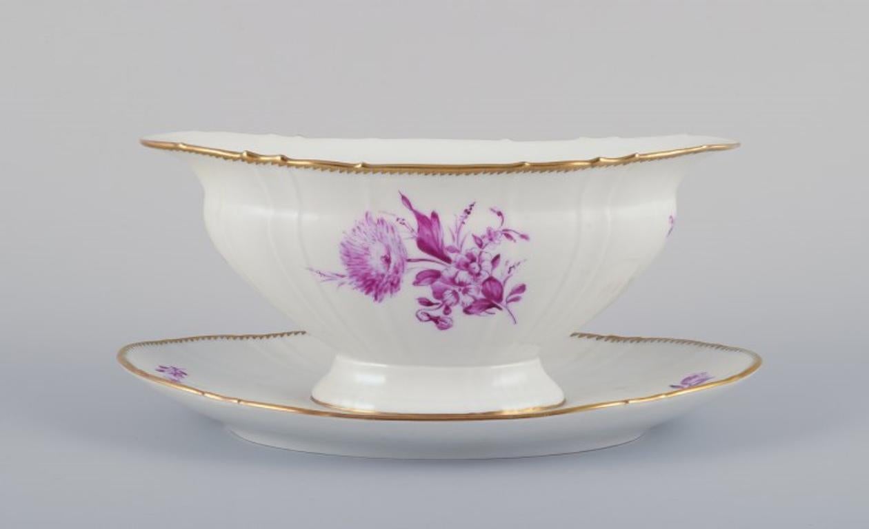 Bing & Grøndahl, Denmark. 
Hand-painted sauce boat in porcelain with floral decorations in purple and gold trim.
Approximately from the 1920s.
Marked.
In perfect condition. Appears unused.
First factory quality.
Dimensions: Height 10.0 cm x Length