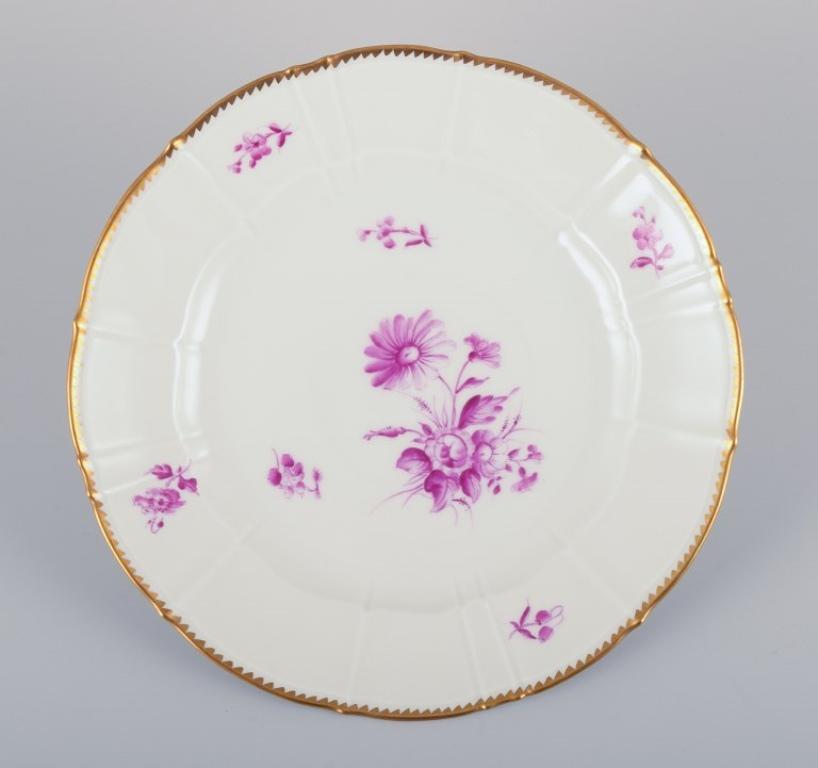 Bing & Grøndahl, Denmark. 
A set of six dinner plates with flower decorations in purple and gold trim. Hand-painted.
Approximately 1920s.
Marked.
In perfect condition. Appears unused.
First factory quality.
Diameter 24.5 cm.