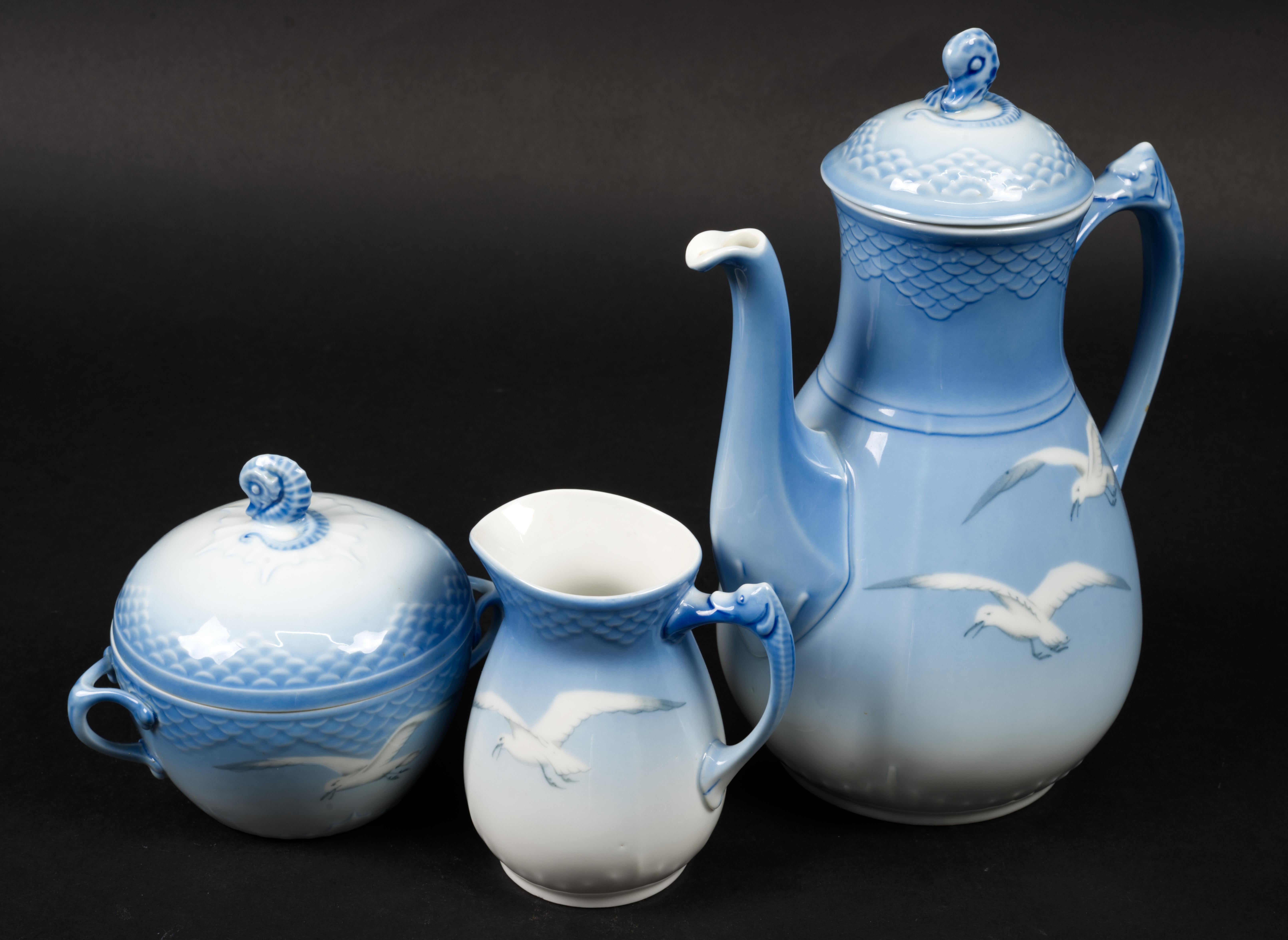 
Bing & Grondahl Seagull coffee service set consists of coffee pot, creamer, and covered sugar bowl.

Reliefs of scales on the rim and handles of the pieces and on the lids are shaded in pale blue with ombre effect; creamer and coffee pot have