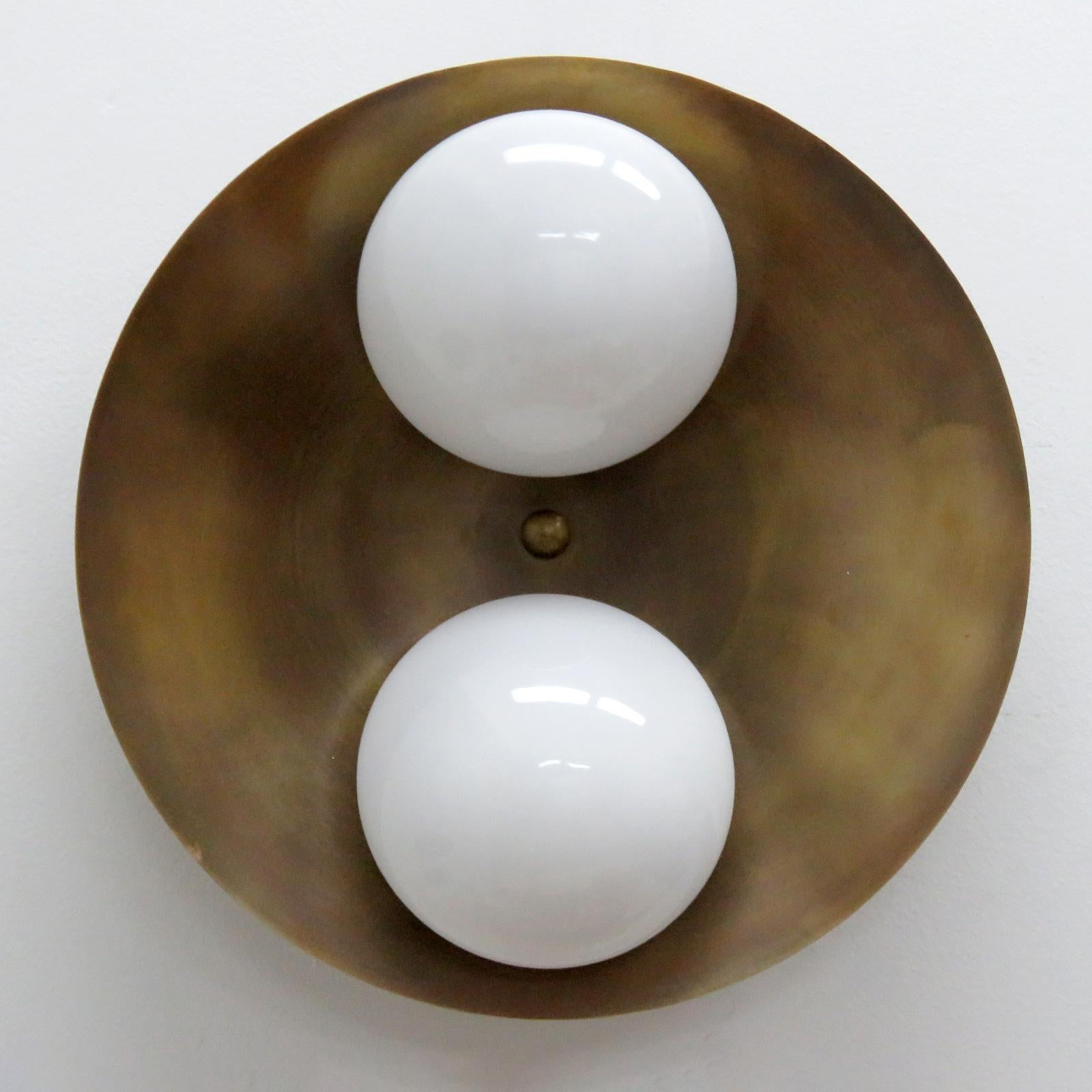 Elegant Binova wall or ceiling light designed by Gallery L7, handcrafted and finished in Los Angeles from American brass, with two opaline glass shades on an aged raw brass disc. Two E12 sockets per fixture, max. wattage 60w each, wired for US