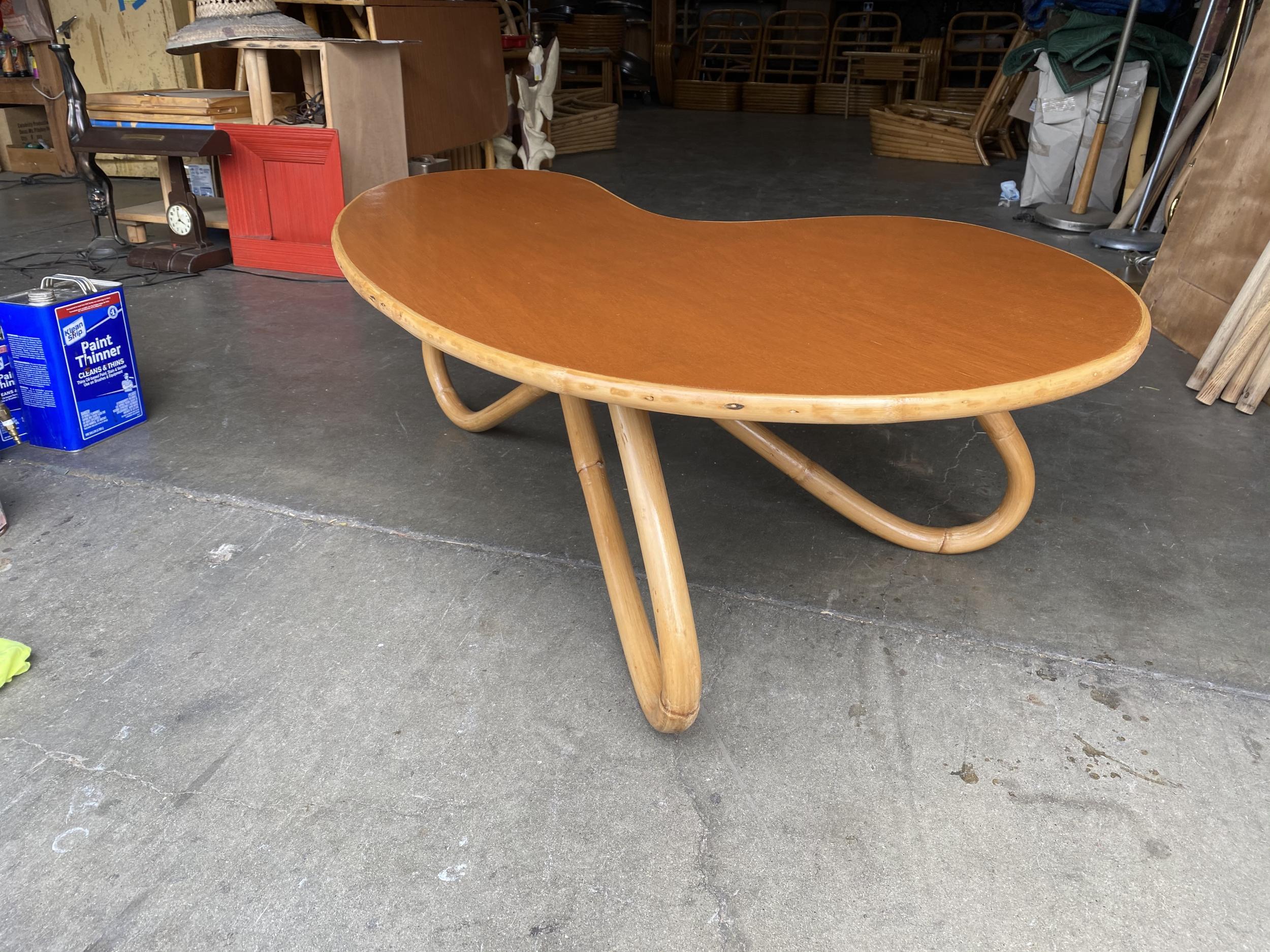 Biomorphic coffee table with loop rattan legs and a mahogany wood top with a rattan trim along the borders.

Restored to new for you.

All rattan, bamboo and wicker furniture has been painstakingly refurbished to the highest standards with the