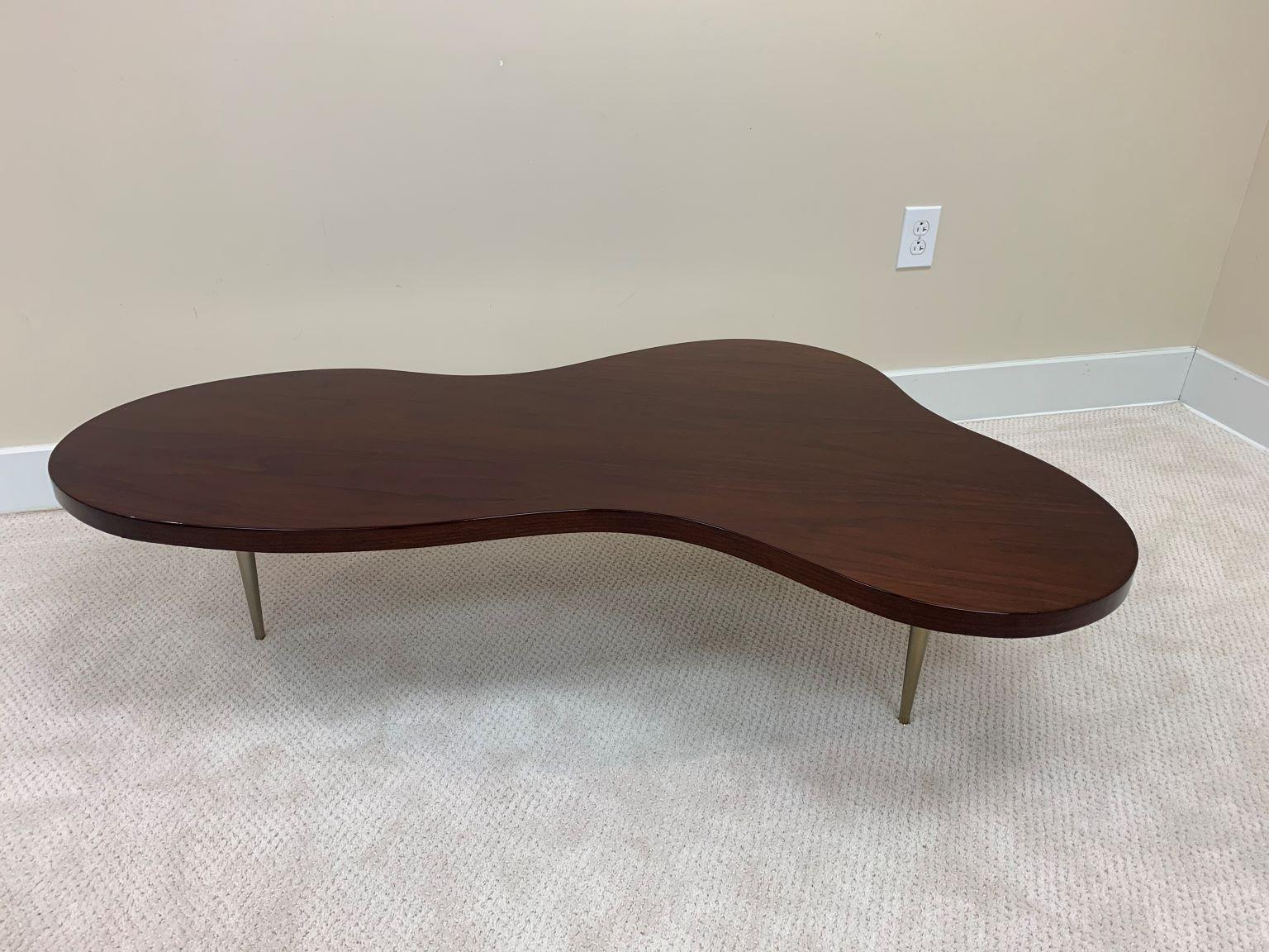 An iconic biomorphic cocktail table in walnut with tapered brass legs by T.H. Robsjohn-Gibbings. The design was produced by Widdicomb Furniture, original label can be found on the underside of the table. Beautifully restored in a gloss finish with