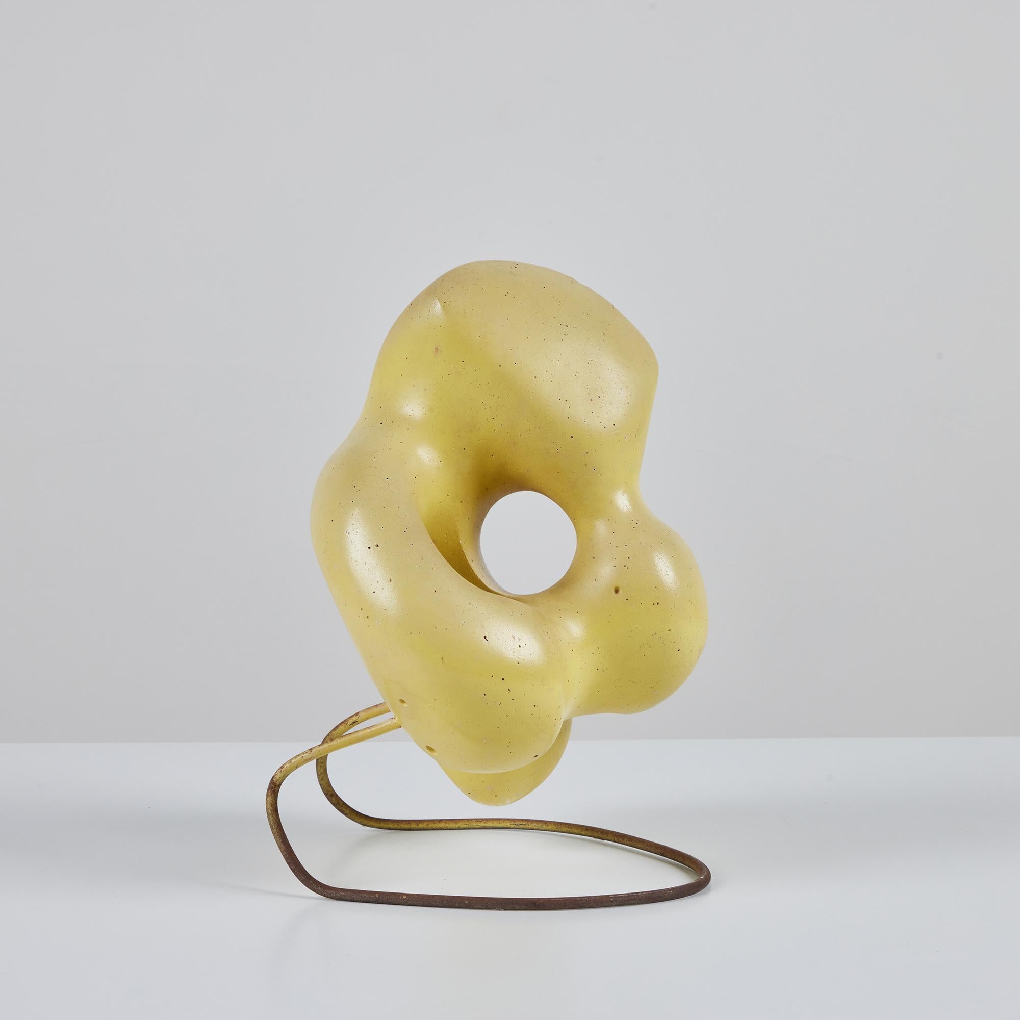 Biomorphic plaster sculpture supported by a curved metal base. This sculpture features soft curves and a pale yellow glaze. 

Dimensions
9.5