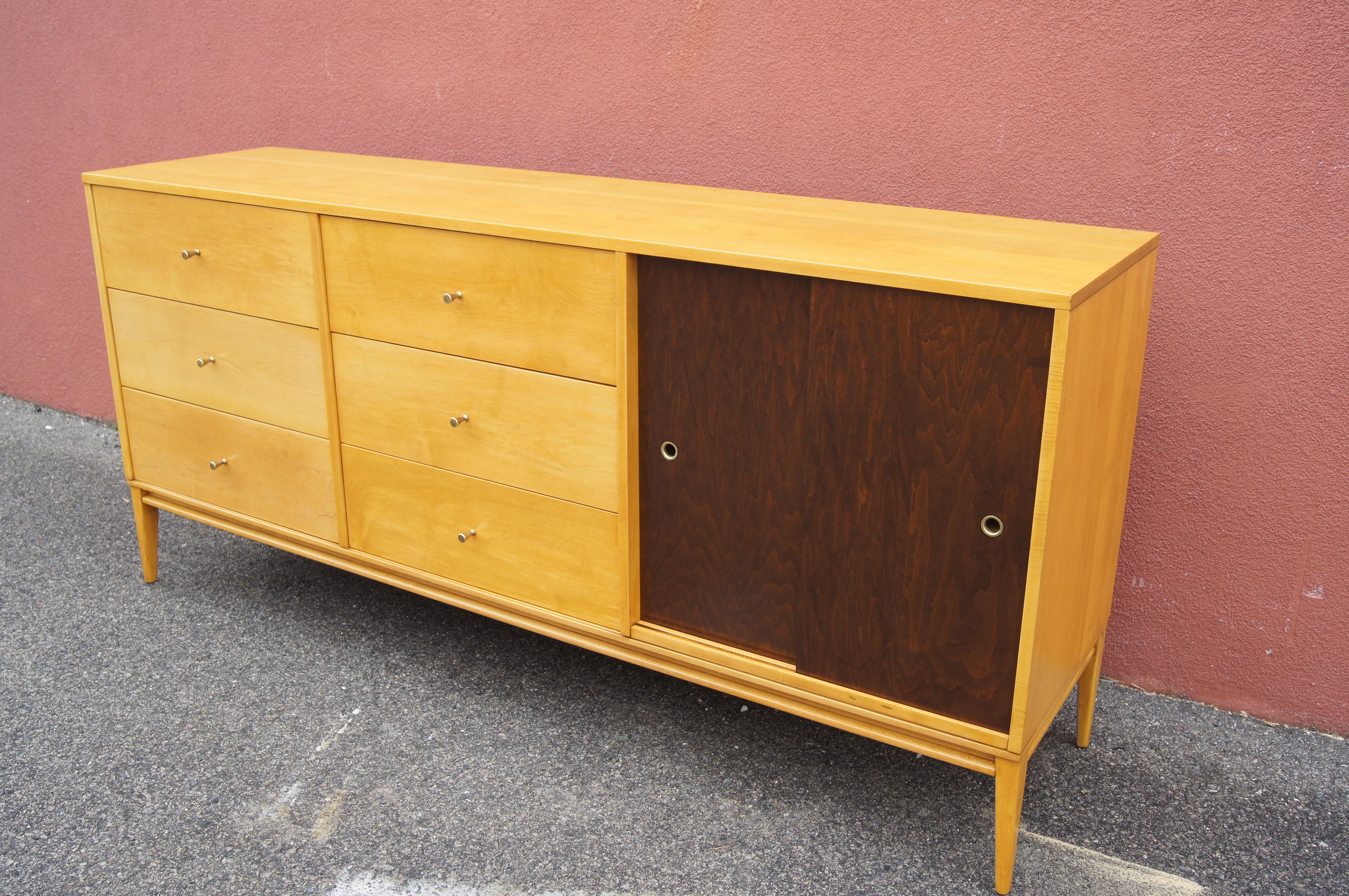 Designed by Paul McCobb for Winchendon's Planner Group, this birch cabinet features two rows of three deep drawers with conical brass pulls and an adjustable shelf behind sliding doors stained a contrasting walnut.
 