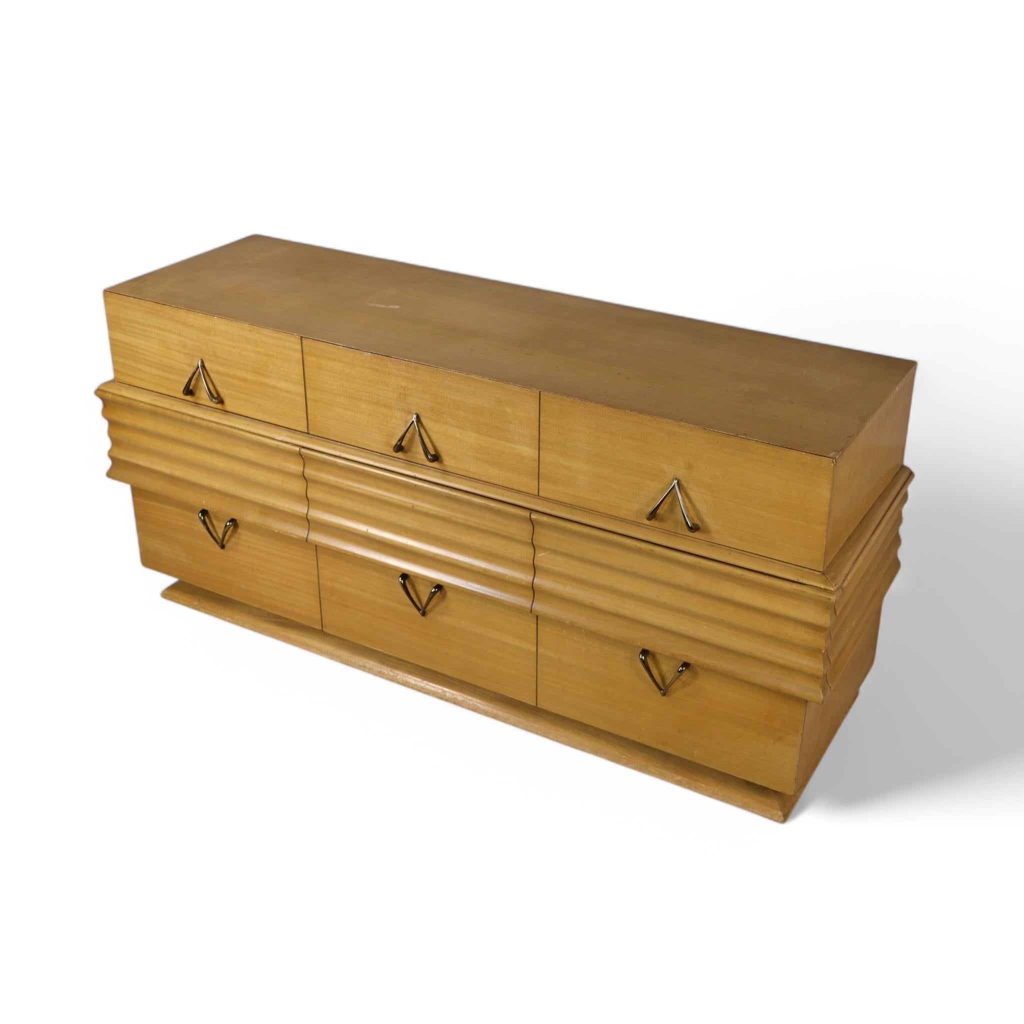 Cette commode basse à neuf tiroirs datant des années 1950 illustre le design moderne du milieu du siècle avec une touche d'influence Streamline Moderne. Ses lignes épurées sont complétées par des détails sculptés et nervurés qui s'étendent