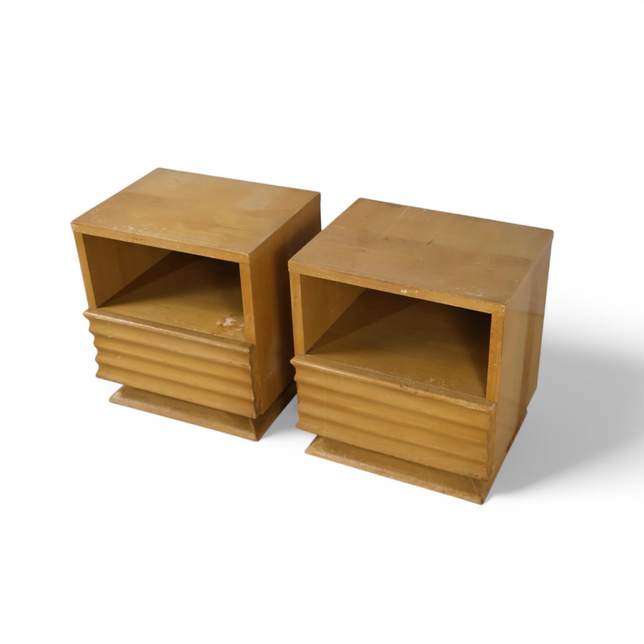 This pair of vintage nightstands showcases mid-century modern design with Streamline Moderne elements, combining practicality with visual appeal. Each nightstand features a clean, boxy silhouette accented by sculpted ribbed detailing on the drawer
