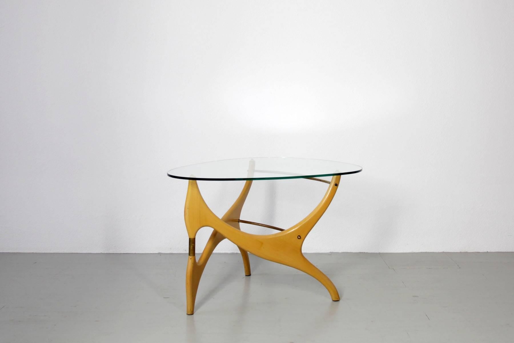 Side or couch table, Italy, 1950s. The table is made out of birchwood and reminds of designs by Carlo Mollino. The egg-shaped glass top unifies the organic forms. The brass elements become decorative element and necessary structural element for the