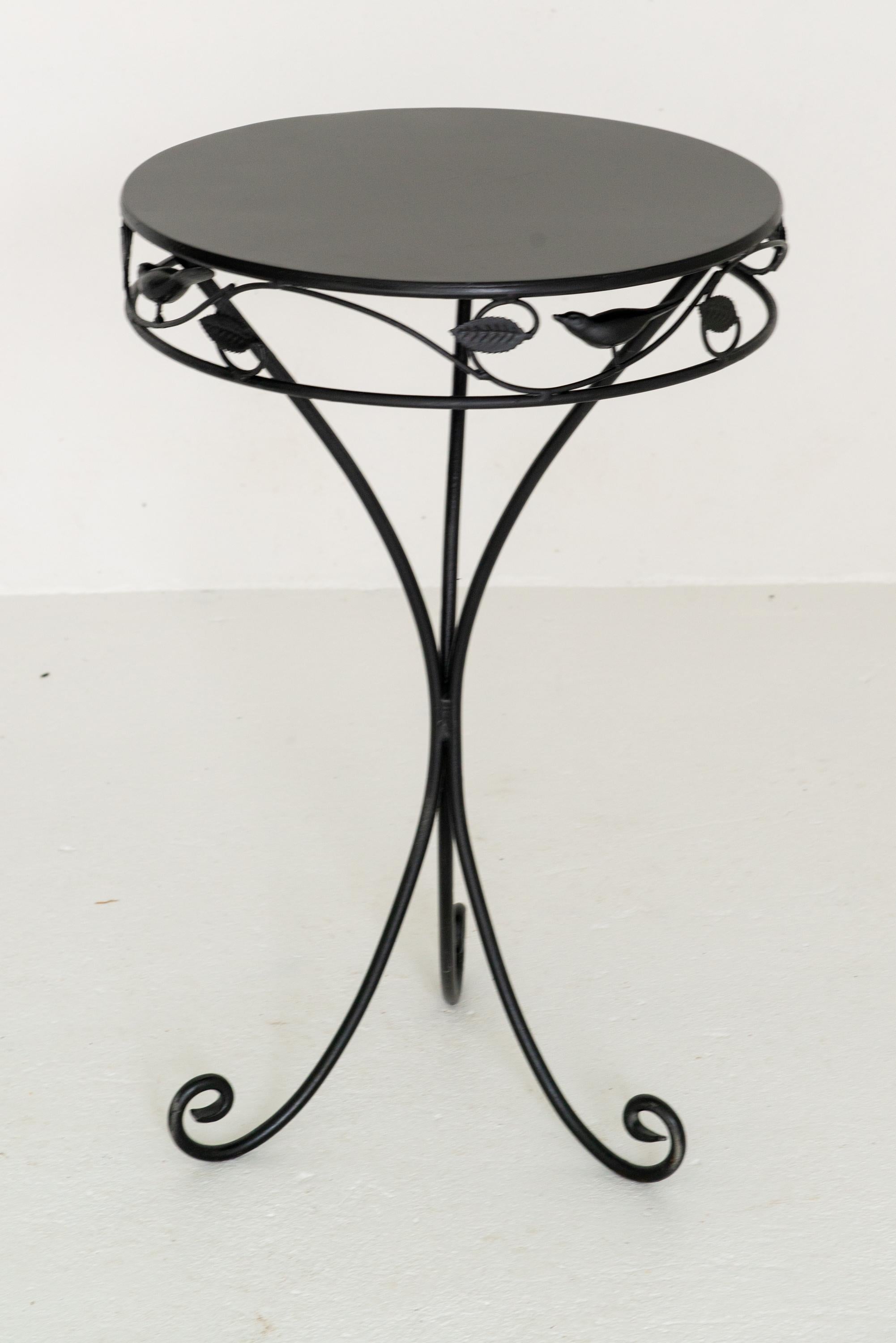 An unusual small round garden side table in black. The table apron is decorated with leaves and three dimensional birds. 