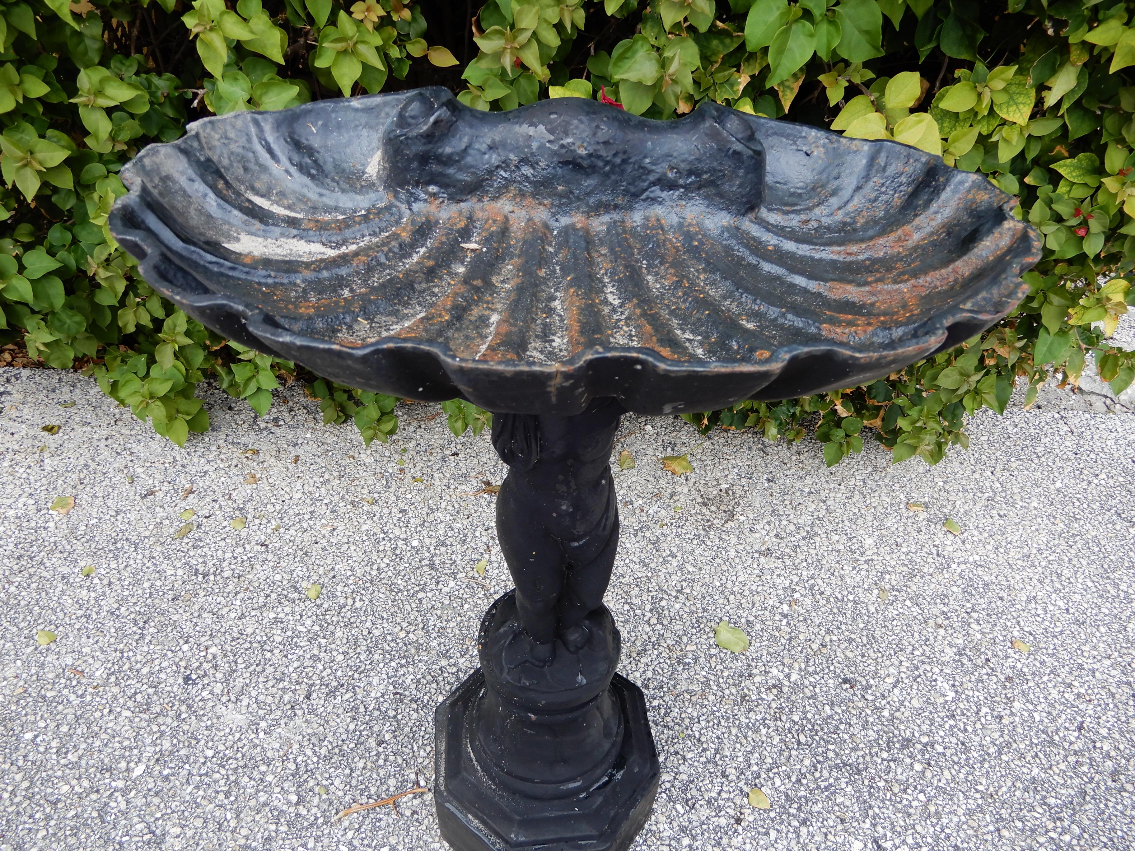 A Victorian cast iron bird bath. The large shell is used to hold the water. The shell is held up by the cherub raised on a platform. The bird bath has an old painted possibly original finish.