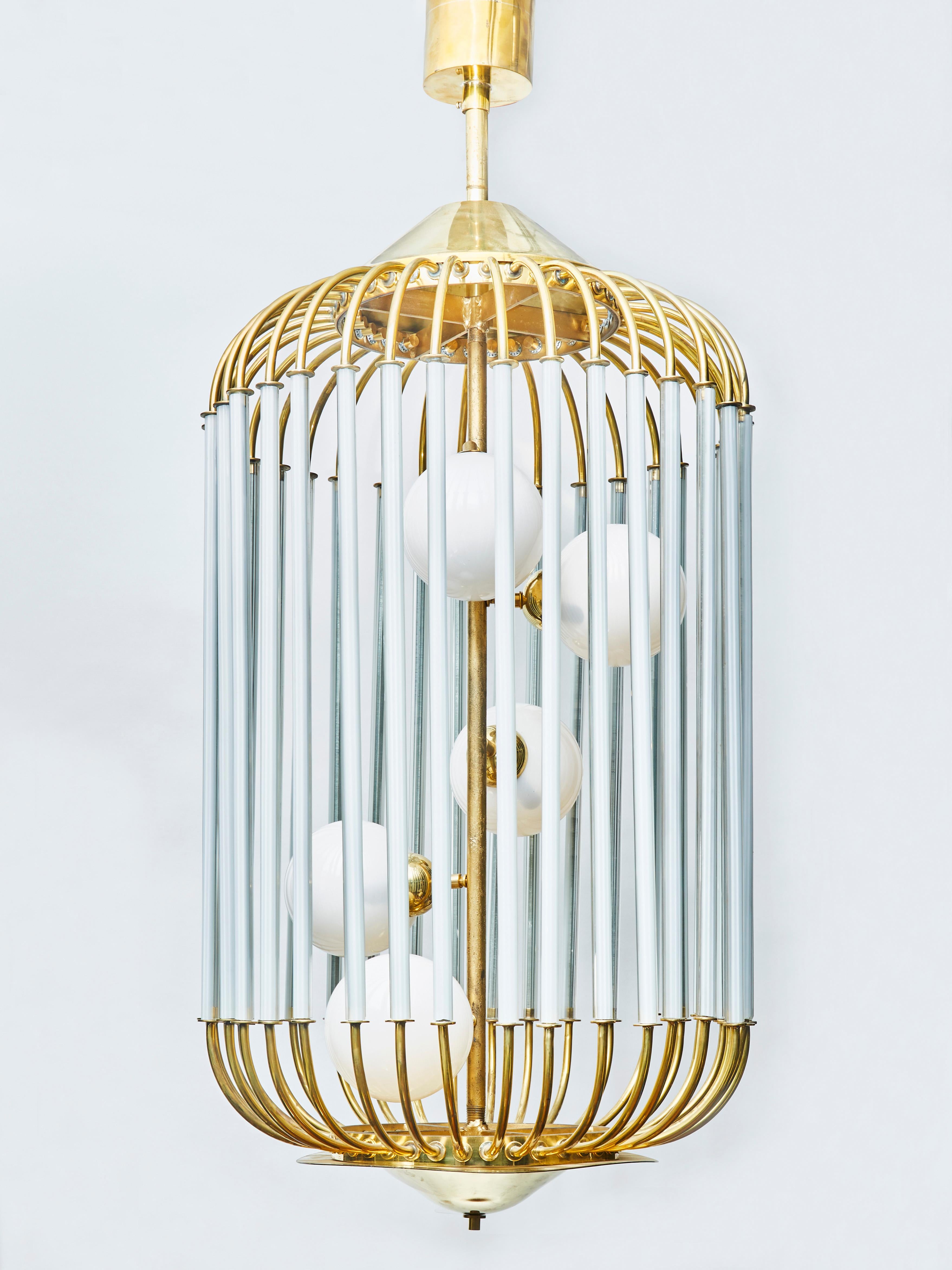 Particularly original chandelier shaped like a bird cage, tinted glass sleeves around the bars circling around a central stem holding five-light in white glass globes.