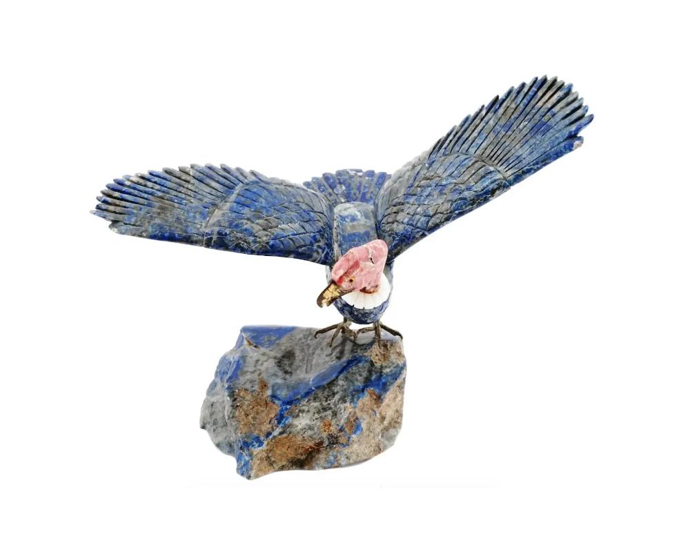 A Mid century hand carved Lapis Lazuli sculpture. The sculpture depicts a bird with open wings. The sculpture is adorned with a hand carved Rhodonite head, encrusted with Amber stone eyes, and gilt brass elements, a beak, and claws. The sculpture is
