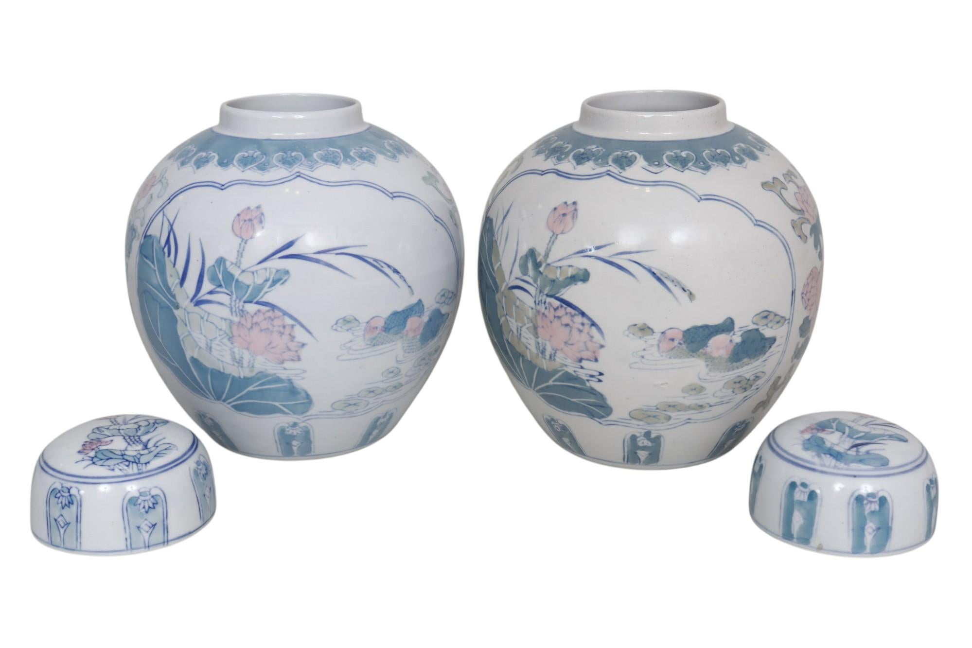 A pair of Chinese lidded ceramic ginger jars. Hand-painted and decorated with two panels of birds and lilies in green and pink. The vases are framed with a foliage motif around the neck and have lily topped cartouches around the base. Dimensions per