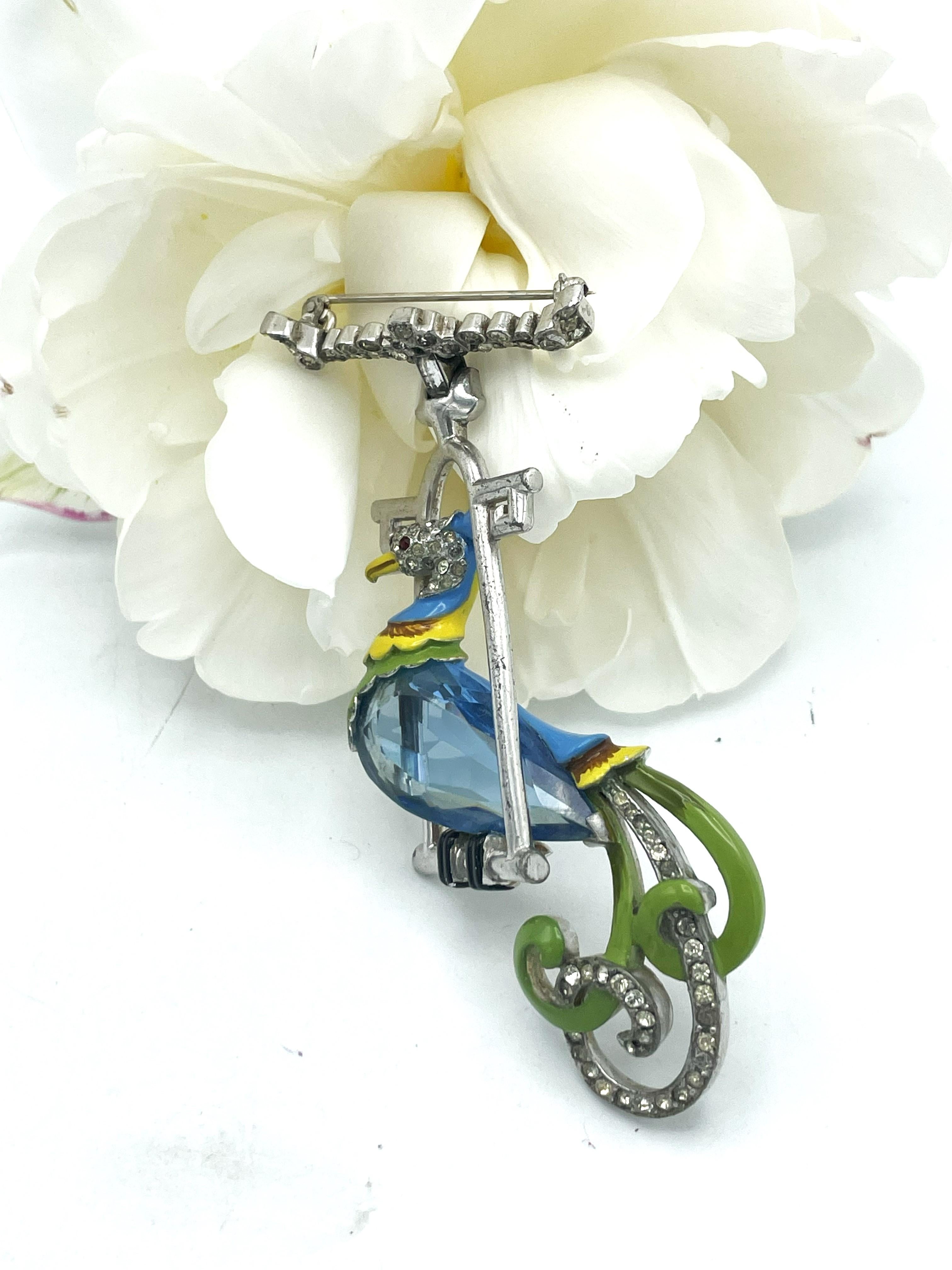 An  aqua bird of paradis on a swing are pendant from the pave crown wich hold die brooch.

Size: 
Height 9 cm
Width   5 cm
Depth  1 cm

Features
- Bird of Paradis sitting on a swing by Mazer unsigned 
- Designed in the 1942s USA
- Polished large
