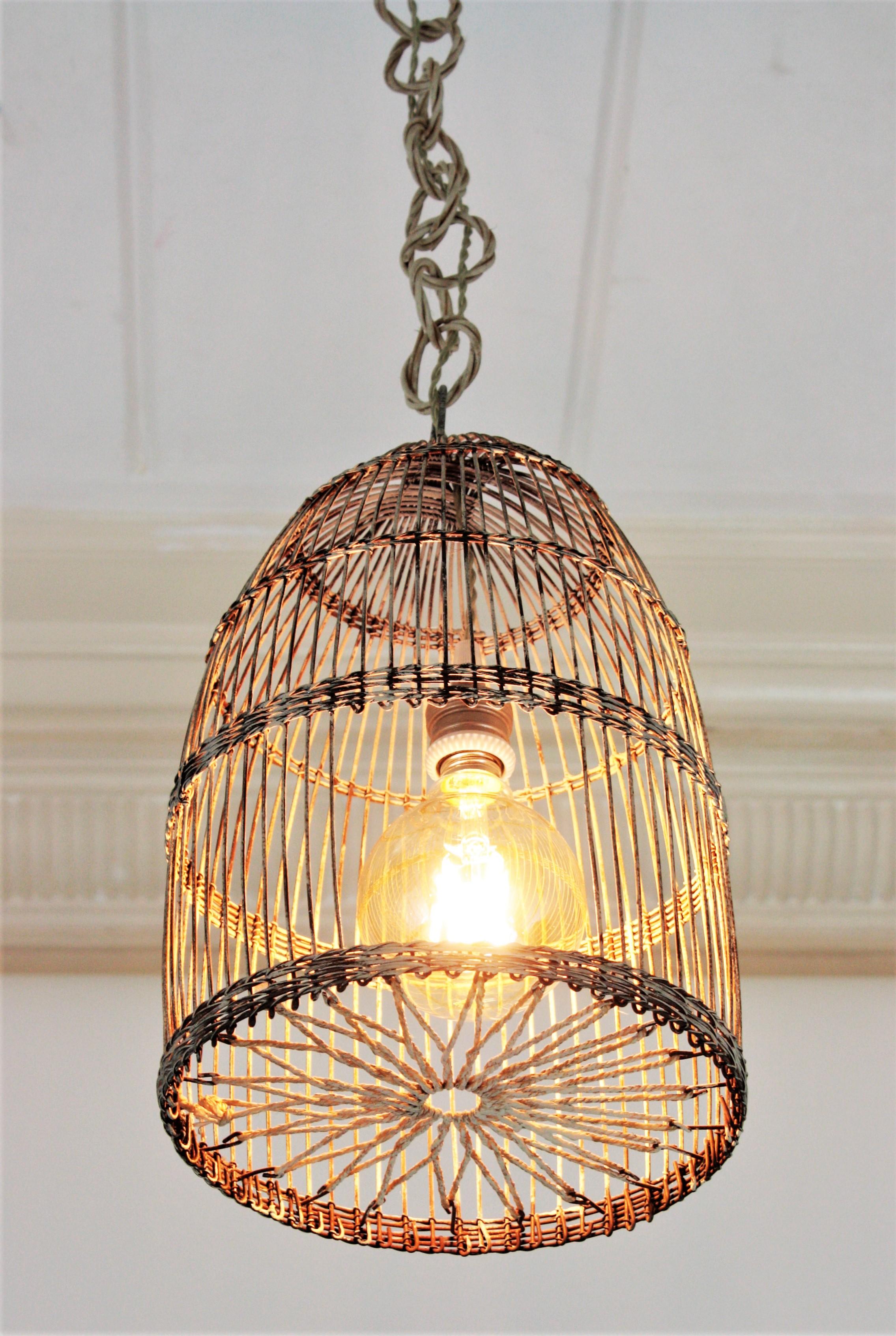 Lovely iron birdcage lantern or suspension lamp with wicker chain, France, 1940s-1950s.
Handcrafted iron birdcage with a star shaped rope detail at the bottom part and patinated details in white color. It hangs from a wicker / rattan chain that