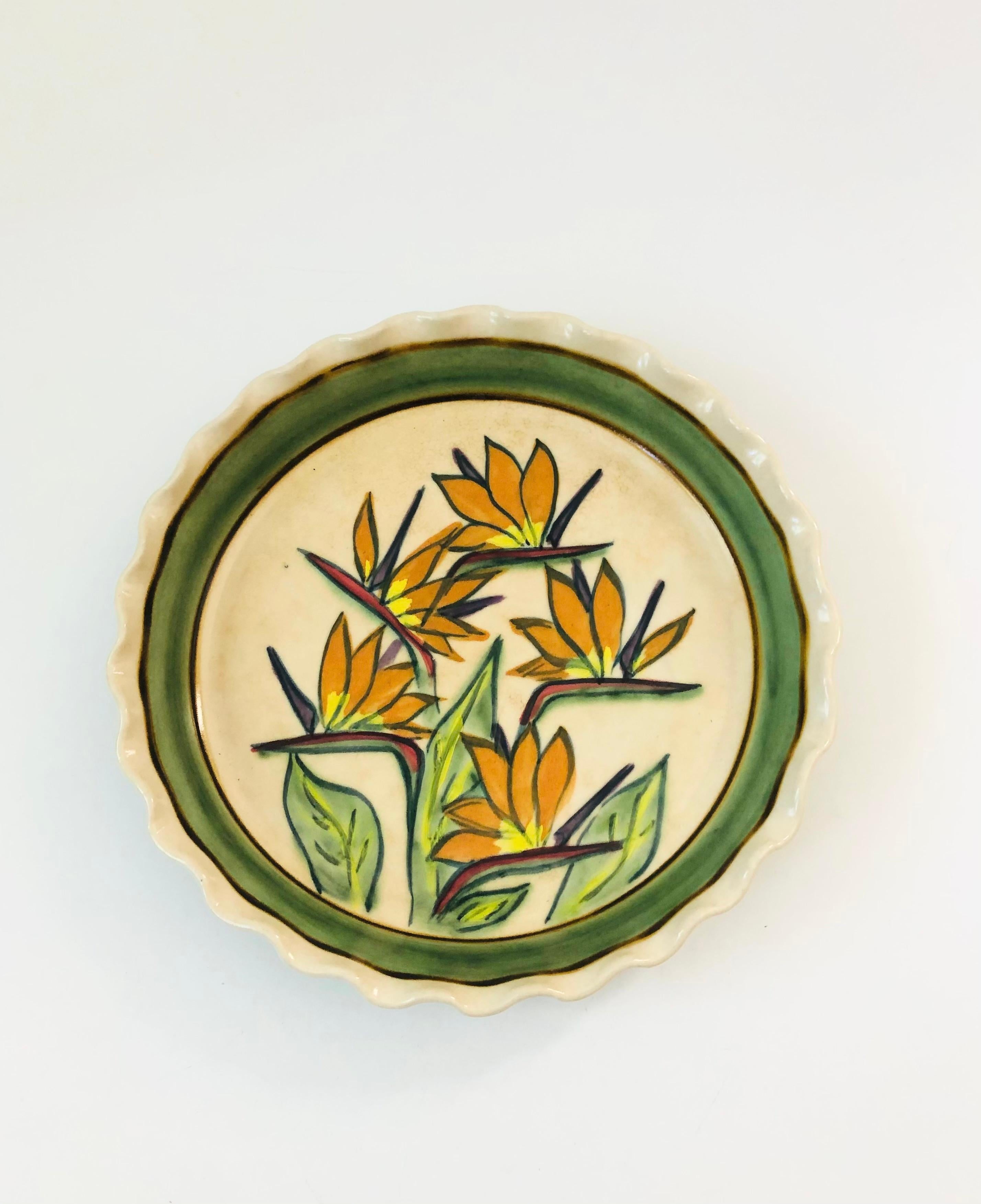 A vintage studio pottery circular pie dish with a beautiful handpainted design in the center of birds of paradise. Lovely curvy edge to the dish. Signed on the base by Adams.

