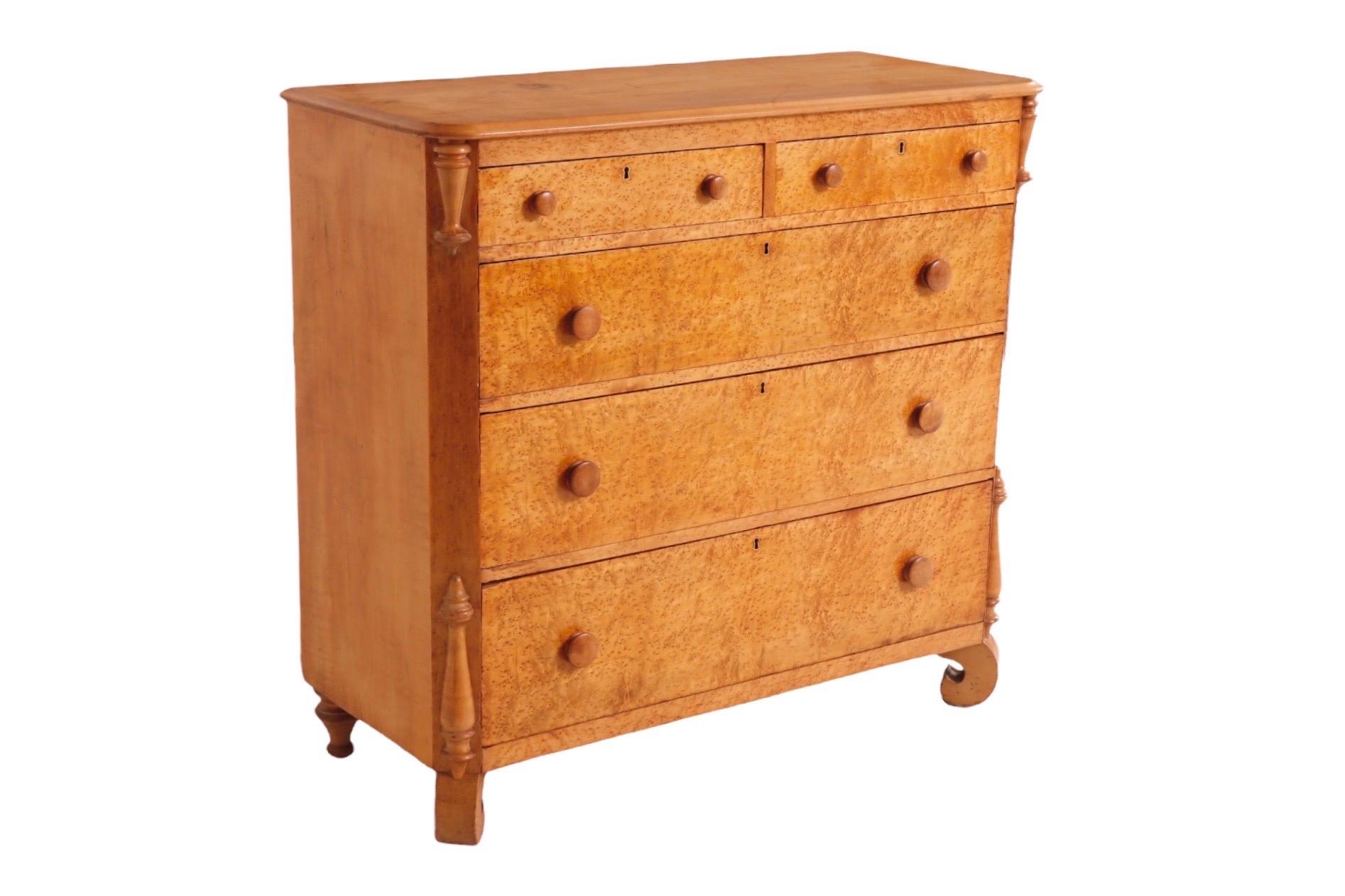 An antique Empire style two over three chest of drawers, decorated in front with birdseye maple veneers. Hand dovetailed drawers open with two round knob handles. The frame is made of blonde maple and decorated with turned appliqués on the corners