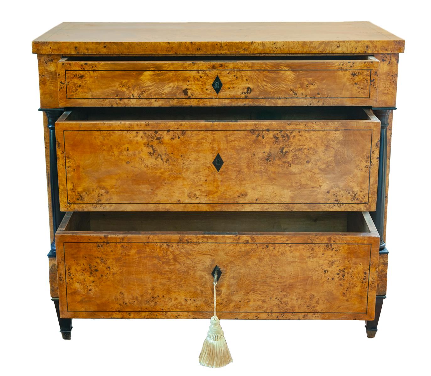 Eine klassische antike Biedermeier Kommode aus blondem Wurzelahorn und Ebenholz.
Die Schubladen werden von Ebenholzsäulen flankiert, die die blonden Holzfurniere und die eingelegten Zierleisten schön zur Geltung bringen. Minimalistische Fassade in