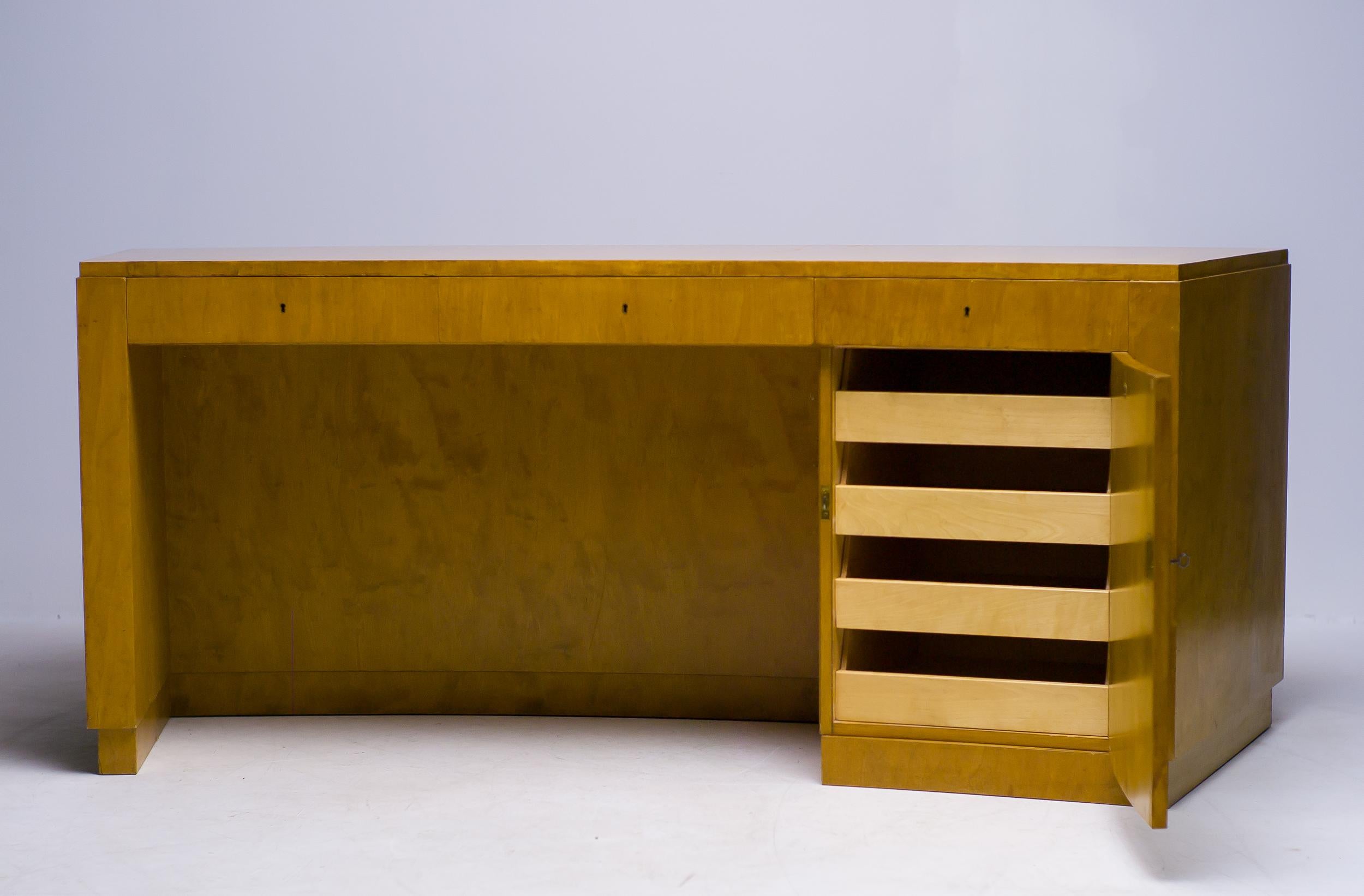 This beautifully streamlined desk is designed by Axel Einar Hjorth for NK in the 1930s. Clad in a pale gold birch veneer (Birka is Swedish for birch) with three locking drawers and a locking door with four concealed drawers. Two shelves are built