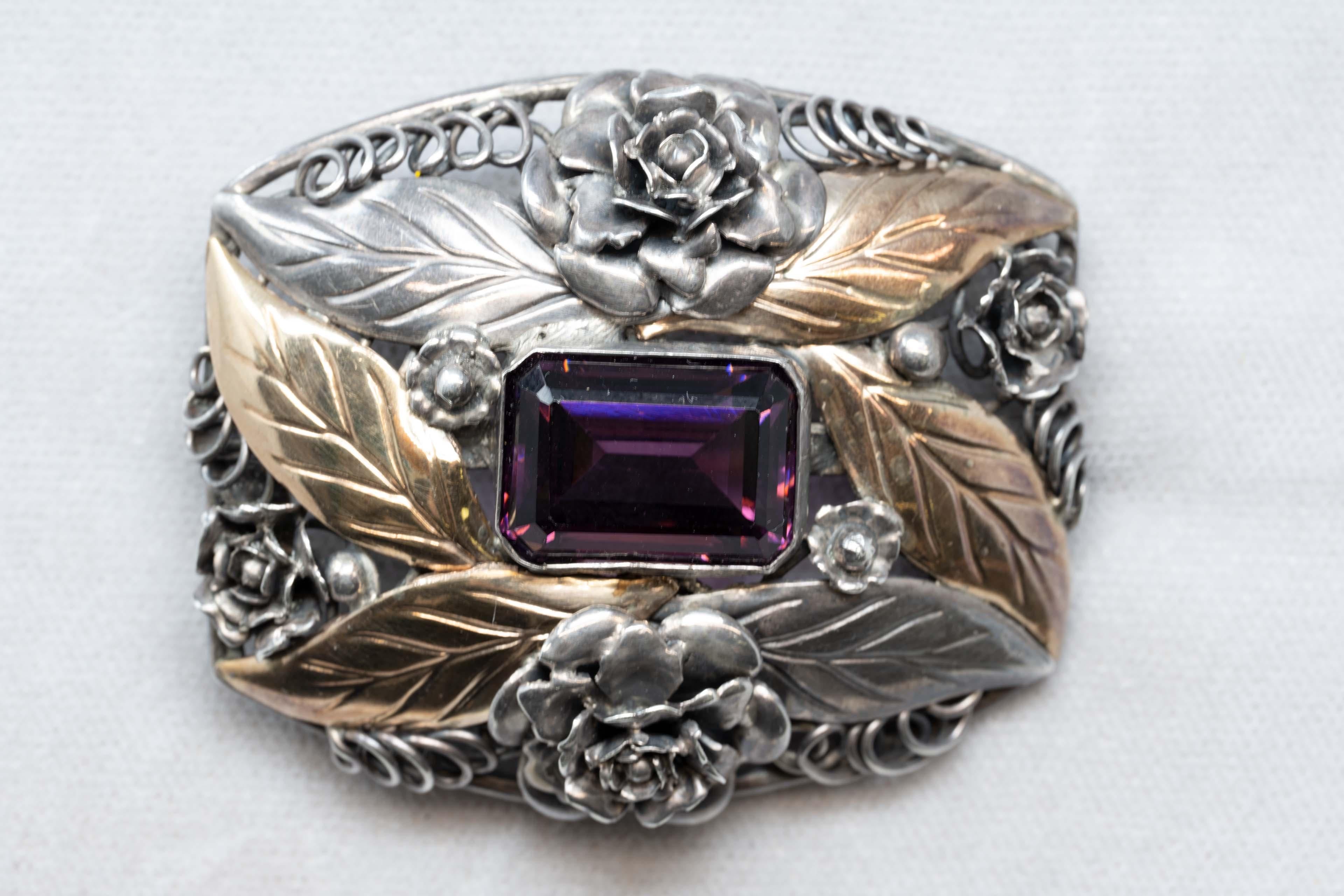 Art Nouveau sterling silver and gold brooch pendant made by Birks. Stamped on the back. Measures 56mm x 47mm, central amethyst color stone measures 15mm x 13mm and flower decoration. Made in Canada c. 1900, in good condition.
