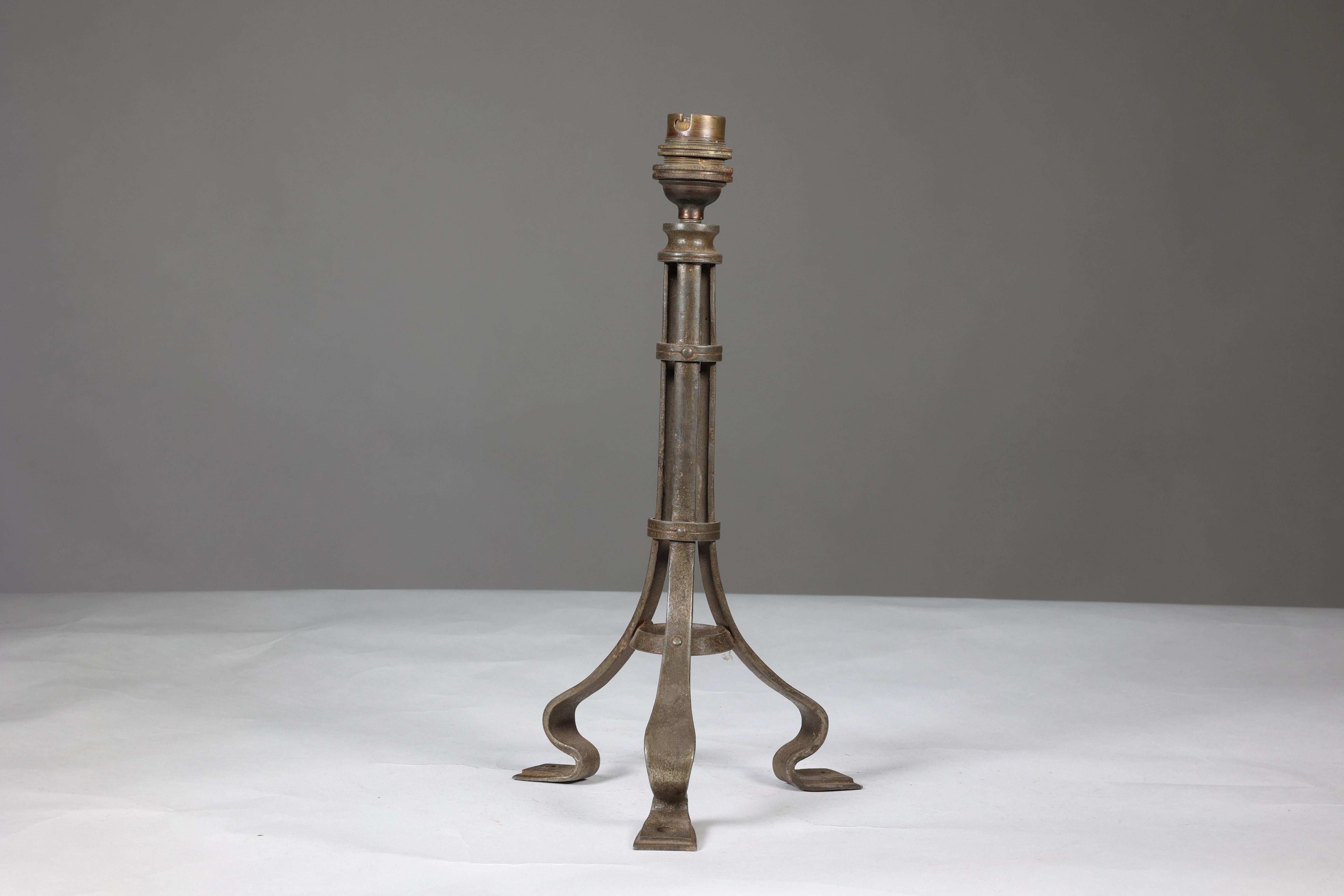 Attribution de la Guild of Handicraft de Birmingham. Lampe de table en fer de style Arts and Crafts, dont le corps principal est constitué de trois supports en forme de balai, réunis par deux anneaux extérieurs et un anneau intérieur vers la base.