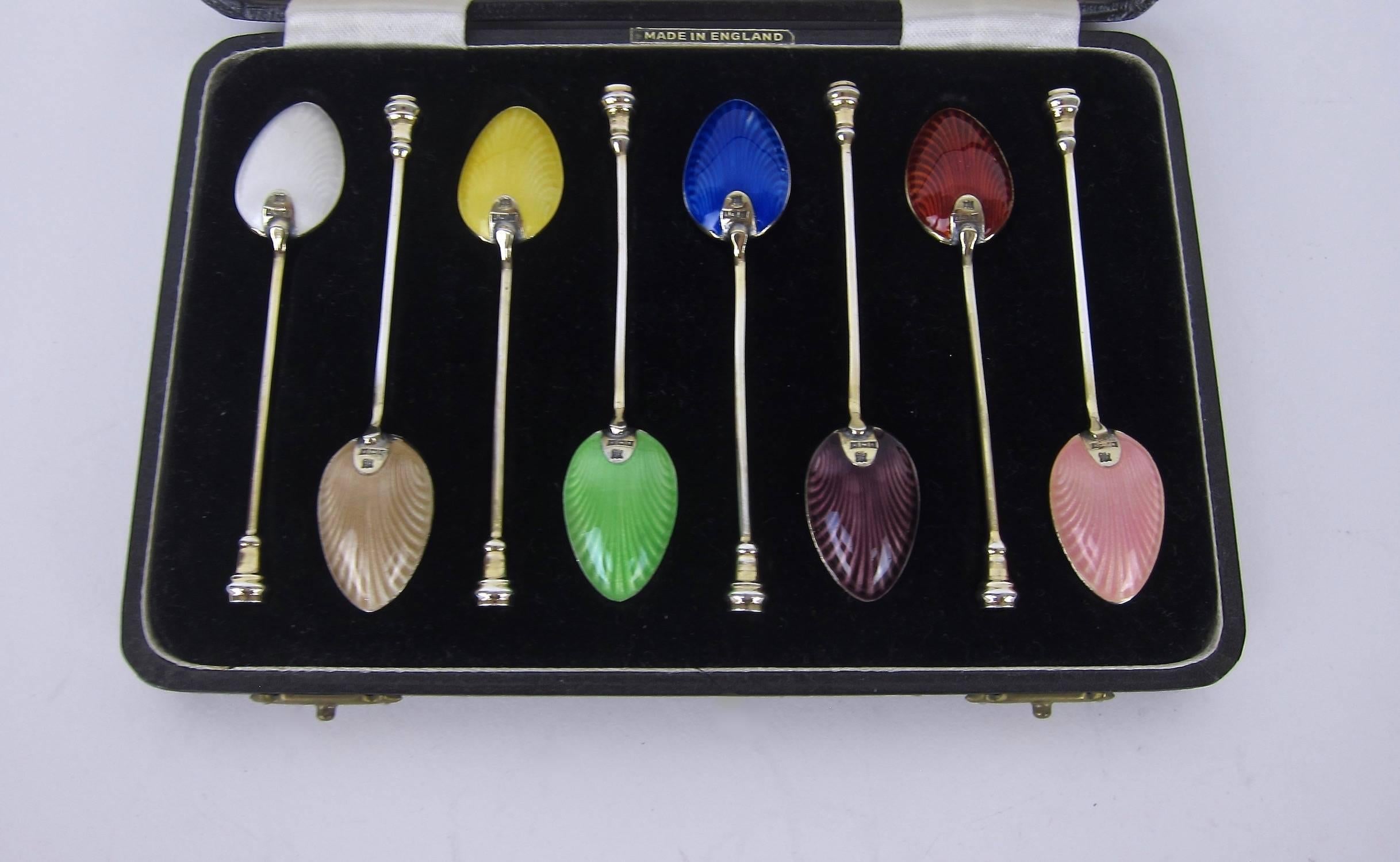A vintage boxed set of eight enameled sterling silver demitasse spoons from the Birmingham Guild of Handicraft. The reverse of each silver spoon bowl is embellished with jewel toned guilloche enamel in a shell pattern, bearing sterling silver