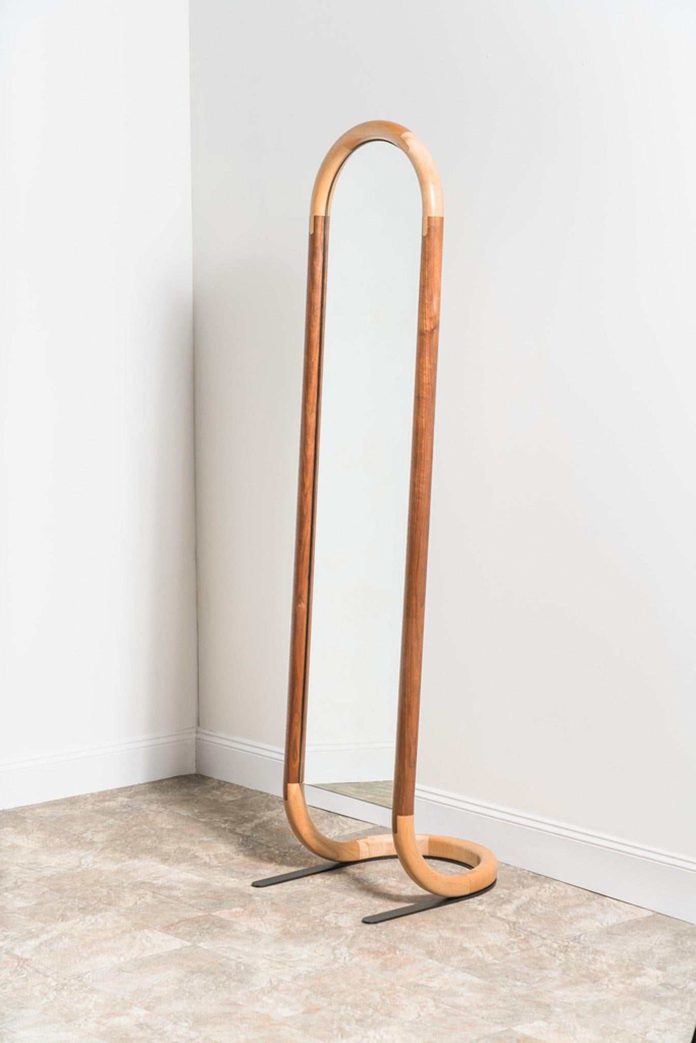 The design of the standing halo mirror relishes in the beauty of joinery. Contrasting wood species emphasize the connections between frame members and the downward arching profile of the mirror seems to mark out the pull of gravity. 

This mirror is