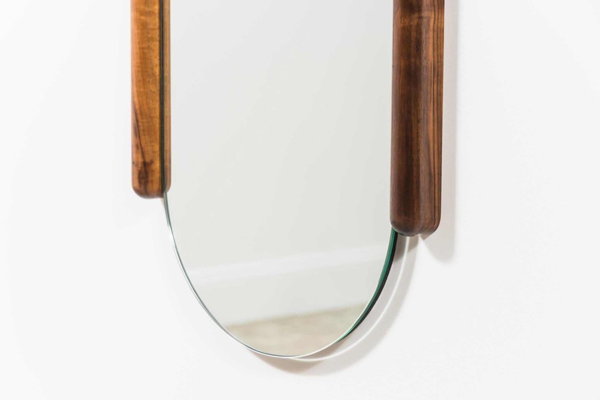 The design of the Tall Halo mirror relishes in the beauty of joinery. Contrasting wood species emphasize the connections between frame members and the downward arcing profile of the mirror seems to mark out the pull of gravity, resisted only by a