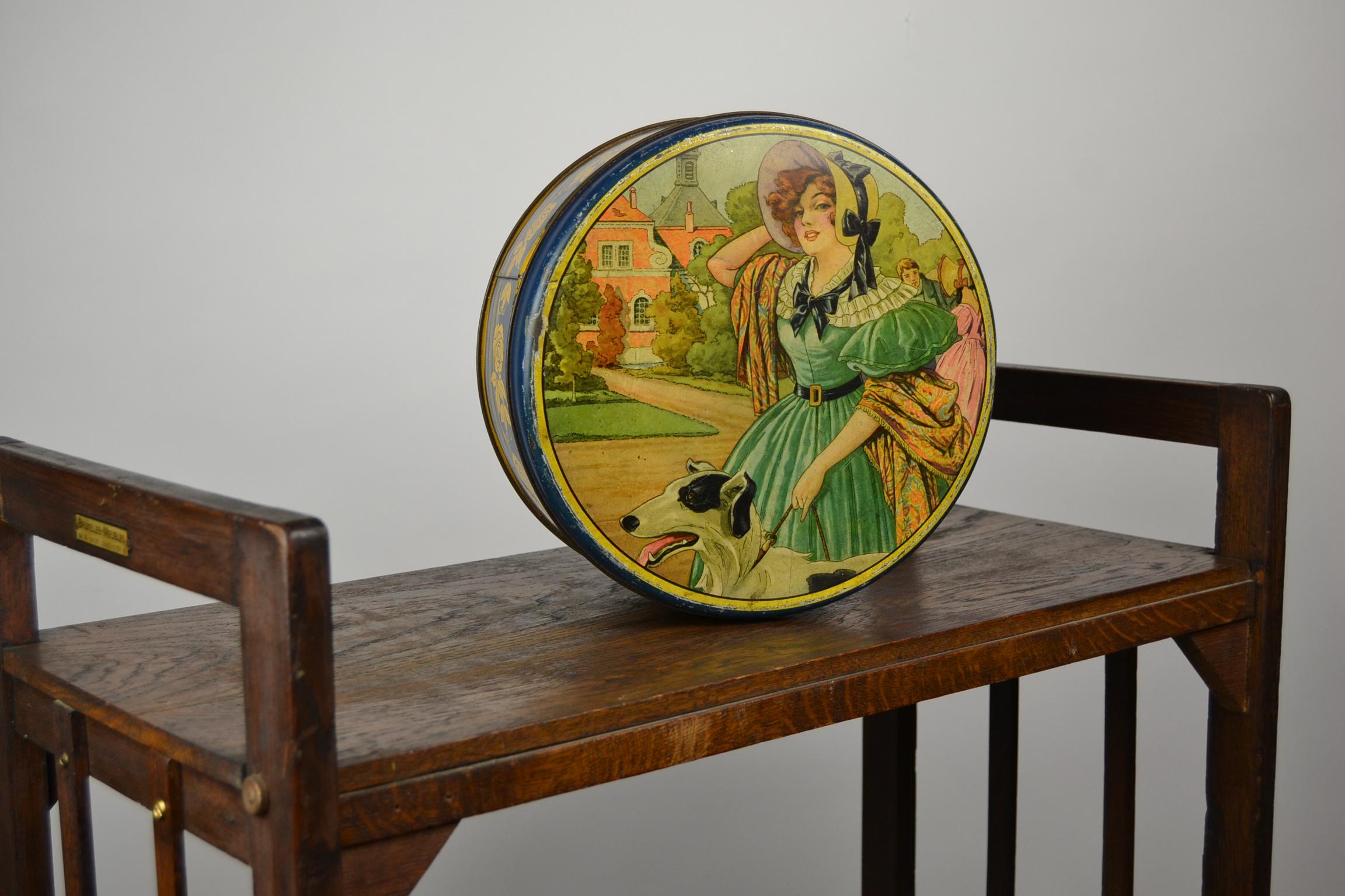 Art Deco large tin with stylish Lithographic design of a Lady and her Greyhond - Whippet Dog , 
having a walk on her estate. 
This biscuit tin - biscuit box was made for Delacre , a Food - Biscuits and Chocolats Factory from Belgium since 1873.