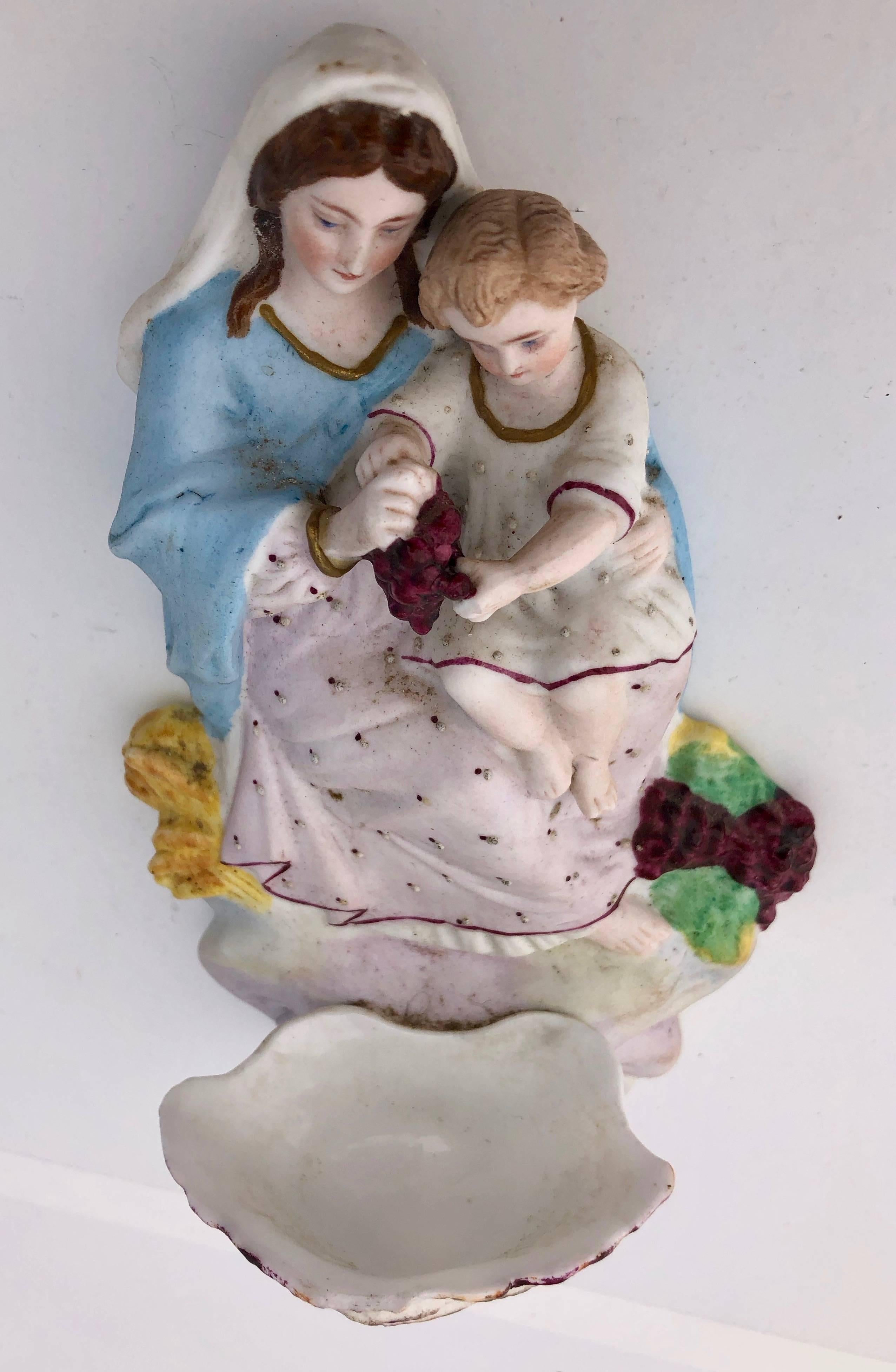 This stunning antique French faïence bénitier is hand-painted bisque in vibrant colors representing Mary and baby Jesus blessing red grapes with a font in the shape of a seashell. It is said in France that such a benetier is believed to offer grape